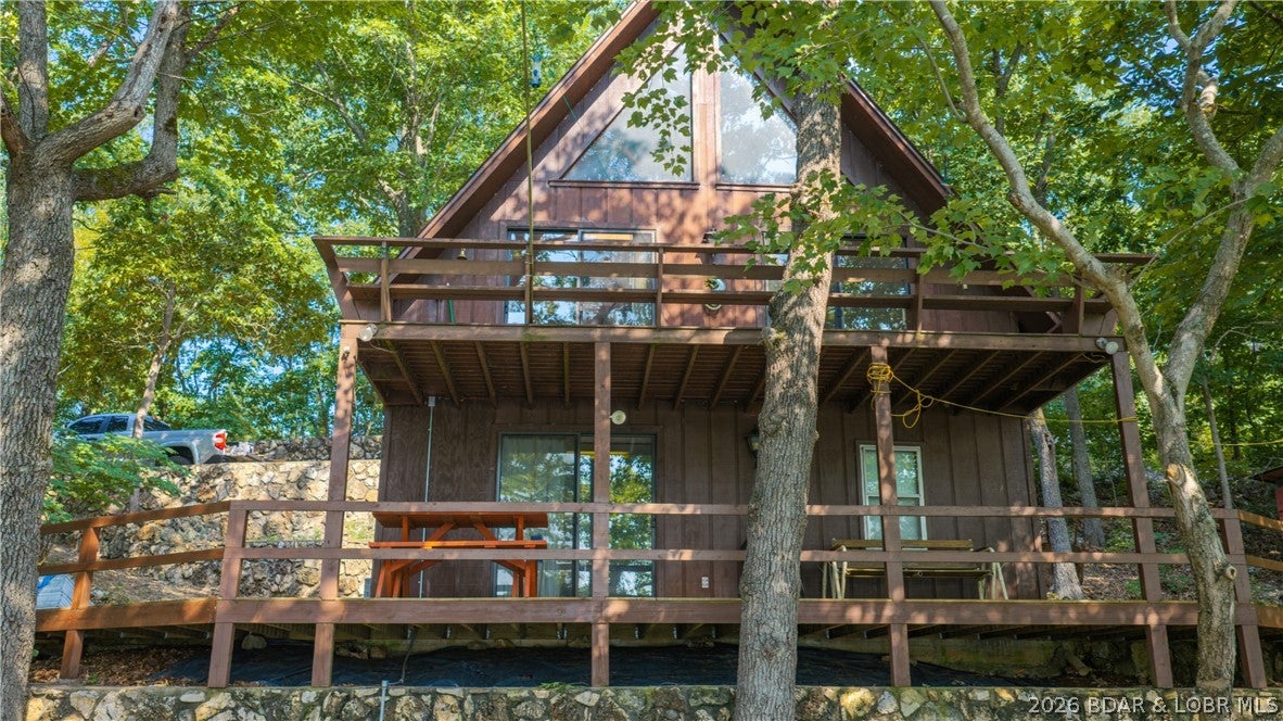 32031 Aurora Road, Stover is the kind of Lake of the Ozarks retreat that feels like an escape the moment you arrive. Tucked among the trees at the 56 MM, this furnished A-frame pairs classic lake-cabin character with 140 feet of shoreline and a covered 2-well dock. Inside, warm wood finishes, soaring vaulted ceilings, a wood-burning stove and large windows create a cozy gathering space with views that keep the lake and surrounding woods close. The main level offers one conforming bedroom and full bath, while the open loft creates additional non-conforming sleeping space. Downstairs, the walkout lower level adds a second full bath, laundry and a flexible great room currently used as another non-conforming sleeping area. Multiple decks invite slow mornings, shaded afternoons and evenings overlooking the water. Down at the shoreline, the dock includes two 10x24 slips, two boat hoists and a PWC slip/lift. With rentals allowed, this property offers the flexibility to enjoy it as a personal lake getaway, investment opportunity or both.