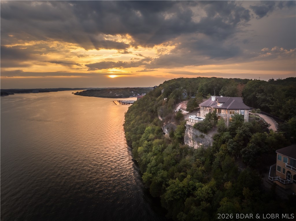 This is one of the finest homes you will find for sale at Lake of the Ozarks. The cost to recreate it today would be significant and the value is obvious the moment you arrive. Situated on 2 premier bluff lots in gated Cedar Crest, the setting delivers unmatched, panoramic views you simply cannot duplicate. That elevated position creates the drama—endless sunsets, total privacy, and a presence that stands out among surrounding luxury homes. With this elevation, you gain something rare: a true estate feel with easy golf cart access to your 16x44 slip in the community dock.  The home itself is exceptional. Built with uncompromising quality, it features a striking stone exterior, a showpiece great room, a custom curved glass-and-iron staircase, and an elevator serving all 3 levels. Every finish was chosen with great thought—Italian handmade furnishings, imported lighting, stone accents, and a stunning marble suite that rivals top resorts. Outdoor living is just as impressive with a 15x40 pool/spa perfectly positioned to capture the view. A private carriage house above the 4-car garage offers a fully separate guest residence. Fully furnished & meticulously maintained, a true showpiece.