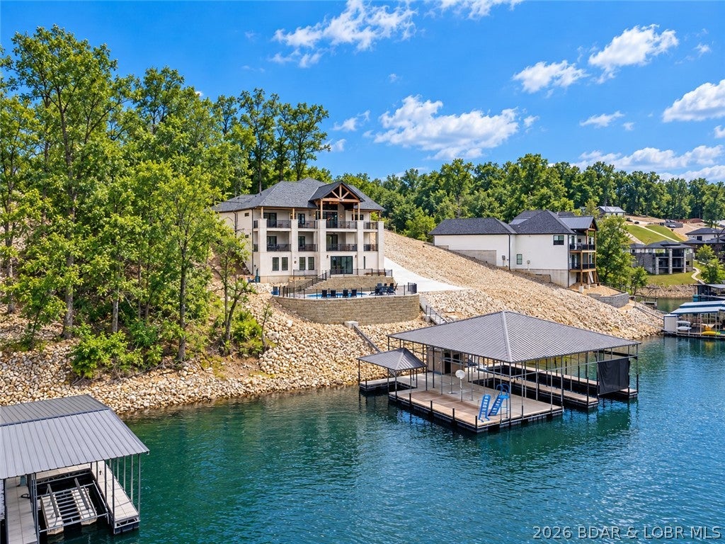 Attention INVESTORS: Luxury lake living with the COMPLETE PACKAGE—POOL, BIG-BOAT DOCK, DEEP WATER, AND GARAGE SPACE! This brand-new lakefront home offers soaring ceilings, walls of windows, expansive concrete decks & incredible views. The gourmet kitchen features high-end appliances, formal dining & a breakfast nook. The lakeside primary suite includes a spa-like bath, large walk-in closet & laundry access, plus 2 additional en-suite bedrooms on the main level. Downstairs you'll find a family room, 3 more bedrooms (one en-suite), custom wine cellar, second laundry & abundant storage. The pool room with bar & full bath opens directly to the 13x27 pool and spacious deck. Exceptional dock setup includes a 16x50 slip, 12x36 slip, PWC slip & a filled-in 12x50 slip that can be converted for a performance boat. Oversized 3-car garage, extra parking, 10' golf-cart path to the water with turn around area, deep-water cove, city water/sewer & quick main-channel access. Rental projections exceed $250,000. Owners have priced this to sell. Call for to schedule your private tour TODAY!