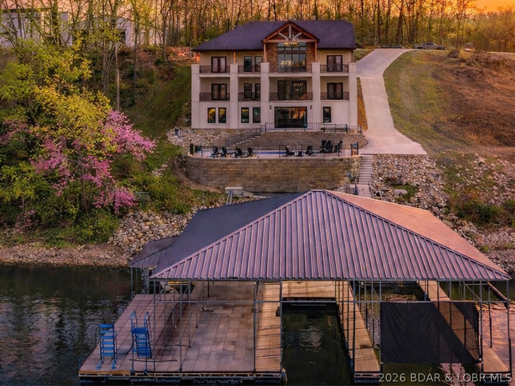Stunning brand-new lakefront home offering the ultimate in luxury living. Grand entry welcomes you with soaring ceilings & a wall of windows with breathtaking views. The great room flows seamlessly into a gourmet kitchen w/ high-end appliances, formal dining, & a kitchen nook leading to expansive concrete decks. The lakeside primary suite features a spa-like bath, large walk-in closet, & access to the laundry room. The main level offers an additional lakeside suite & a third en-suite bedroom. Lower level includes a family room, three additional bedrooms (one Suite), 1/2 bathrm, a bonus room w/ custom wine cellar, second laundry, & ample storage. The pool room w/ bar, full bath, & storage opens directly to the 13x27 pool & large deck area. Dock featuring a 16x50 slip, 12x36 slip, PWC slip, & a filled-in 12x50 slip easily convertible for a performance boat. Oversized 3-car garage plus additional parking, 10’ golf cart path w/ turnaround at the water’s edge, deep-water cove, city water & sewer, & quick access to the main channel & amenities. Ideal as a luxury rental or executive retreat (see attched projections). Optional second-tier Lot 46 available—perfect for a guest home/man cave.