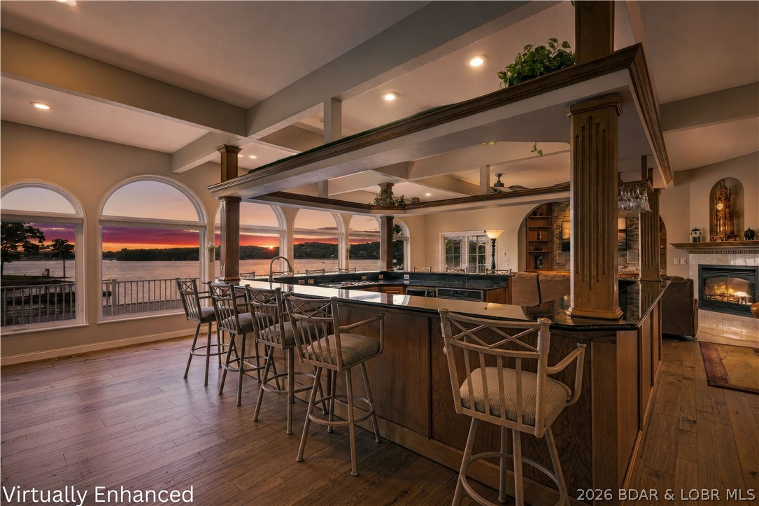 Being able to socialize in your own home has never been easier! The open-bar living concept is exceptional for family and entertaining. This contemporary lakefront home offers 97 feet of gentle shoreline, a concrete seawall with rip rap, and a private dock featuring a 12x28 slip, dual PWC wells, and dockside storage. It is ideally located across the water from Margaritaville and LandShark Bar & Grill. Designed for comfort, both levels are accessible by elevator and filled with natural light and main channel views. The main level presents an open layout with arched windows, warm wood accents, and a sunroom for year-round enjoyment. The kitchen is anchored by an expansive bar and granite surfaces, complemented by an updated butler’s pantry with quartz counters and pull-outs. The primary suite is privately situated with a walk-in shower, radiant heated bath floors, & a spacious closet with its own washer and dryer. The walkout lower level offers a second living area, three additional bedrooms—two ensuite—along with a half bath and storage. A Cummins backup generator ensures the home is prepared for anything. Outdoor spaces: covered lakeside deck, a fenced pet area & lots of parking.