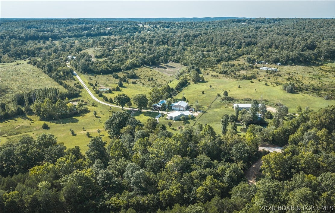Nestled on 12 beautifully manicured acres, this remarkable property offers a rare combination of natural beauty, privacy, tranquility, and exceptional amenities. The property features a year-round peaceful creek, beautiful Ozark bluffs, a stocked pond, and an artesian well, with mature trees creating a stunning park-like setting. Wildlife is abundant, w/ deer & turkey frequently seen throughout the property. The comfortable 3-bed, 2-bath home features an attached 2-car garage, spacious 40x40 attached workshop, and four porches and decks designed to enjoy the peaceful surroundings. One screened-in deck includes a hot tub, perfect for relaxing in any season. The fenced backyard adds convenience & privacy. A beautiful approximately 500sqft guest house with its own 2-car garage provides space for guests, extended family, a private retreat, or additional living space. Despite the secluded setting, you're just 15 minutes from the Lake of the Ozarks, offering shopping, dining, entertainment, boating, fishing, & water sports, plus lake access and Lee C. Fine Memorial Airport. Enjoy nature, entertain family and friends, pursue hobbies in the workshop, or simply relax & listen to the creek.