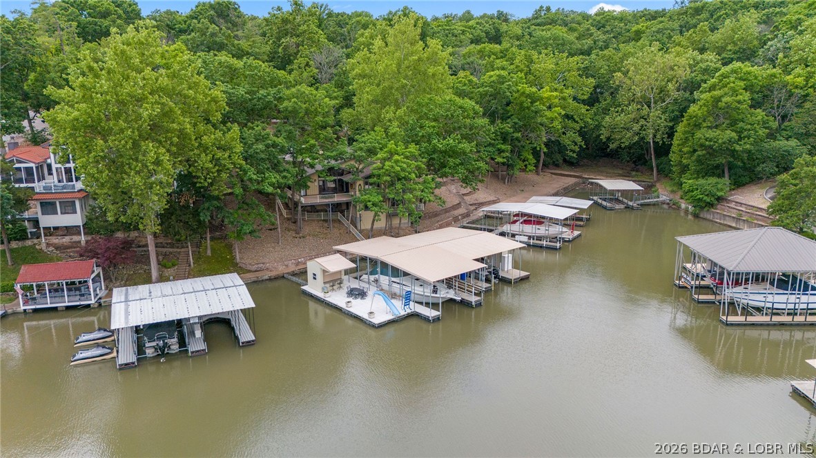 This fully furnished 4 bedroom, 4 bath lakefront home is all about living on the water—perfect as a private retreat or an income-producing vacation rental with nightly rentals allowed. The front door puts you right at the lake, with open and covered decks that invite you to linger over morning coffee and sunset dinners overlooking the water. Inside the main level’s vaulted ceilings and cozy fireplace frame the lake views, while a formal dining room, breakfast bar, and wet bar make it easy to host weekends at the lake. The main level also features an en-suite bedroom with walk-in showers and walk-in closets, giving everyone a comfortable, private place to unwind after a long day on the water, and the lower living room creates an extra hangout spot for family & friends. Just a few steps from the house, a massive dock becomes the heart of your lake life, complete with a bar for dockside gatherings, a water slide, a swim platform for lounging and jumping in, and three boat slips, the largest being a 16' x 50' slip ready for your cruiser or big-water boat. Turn-key and ready to enjoy from day one, this property delivers the easy, laid-back lake lifestyle so many people dream about.