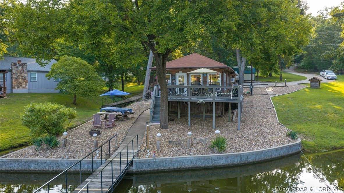 Tucked into beautiful Mill Creek Cove on the Gravois Arm, this is the kind of Lake of the Ozarks setting that’s getting harder to find.
An easy drive from Laurie down the ever popular paved O Rd, this 3 bedroom, 1 bath home sits on a gentle lakefront lot surrounded by mature trees with a beautiful open meadow. The shingled exterior, large lakeside deck & peaceful setting give it that nostalgic lake feel everyone desires, while the spacious 3 well dock is an incredible offering. The current owners have lovingly cared for & impeccably maintained this property. There’s also a carport alongside the home, plenty of outdoor space & a setting that gives you room to enjoy the lake without feeling like you’re sitting on top of your neighbors. You get the best of both worlds here. A peaceful lakefront retreat tucked into one of the most popular pockets of the West Side, with a great lot, beautiful setting & a 3 well dock with 2 boat hoists & 1 twin PWC lift. Opportunities like this in Mill Creek Cove are few & far between. If this is the part of the lake you’ve been waiting for, you’ll want to move quickly.