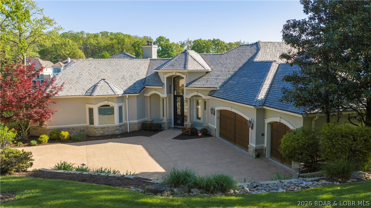 This mediterranean masterpiece features arched accents with columns supports creating grand architectural style. The stucco exterior is accented by stonework along the base, stately iron entry door, rich wood garage doors, and lifetime slate style roof. Once inside the quality and style are evident with open winding staircase and deck showcasing the spectacular pool and lake views. To your right is the open living, dining and kitchen that is an entertainer's dream featuring custom wood cabinets, butler's pantry, formal & informal dining areas and a wall of lakeside windows to enjoy the spectacular view. To your left is the owner's suite that does not disappoint--large spacious suite with fireplace, private deck, spa-like bath and custom walk-in closet. Second full suite, half bath, laundry and elevator access complete the main level. Follow the winding staircase up to stunning suite with balcony overlooking living area. The lower level provides large great room with 2nd full kitchen, lakeside suite, bunk room, and pool bath. Then you enter your outdoor oasis with heated pool and large cruiser dock-all perfectly accented by mature landscaping making this the perfect lake retreat!