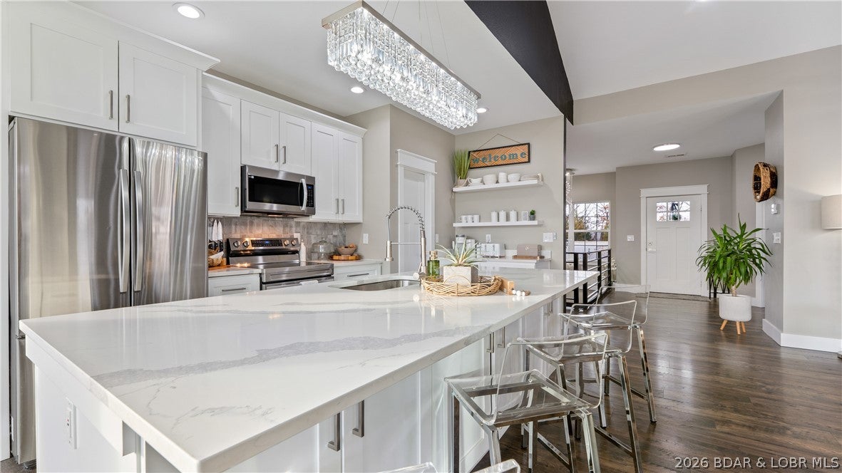 Step into a new chapter in this gorgeous 5-bedroom, 3-bathroom home! Located in a quiet residential neighborhood, you’re just a short walk from a local school, church, and vibrant energy of the iconic Bagnell Dam Strip. Large windows and a grand triple sliding glass door flood the home with natural light while offering seasonal lake views. Designed for effortless flow and effortless hosting, the oversized, chef-inspired kitchen serves as the centerpiece of the home—offering plenty of space for multiple cooks and casual entertaining. Downstairs, the ultimate lower level features a supersized family room, wet bar, full bath, and 3 additional bedrooms. Enjoy the perfect balance: minutes from local dining, shopping, live music, and lake activities, yet tucked away for peace and privacy. Located just a three minute walk of a local marinas. Call your real estate professional today to schedule a showing!