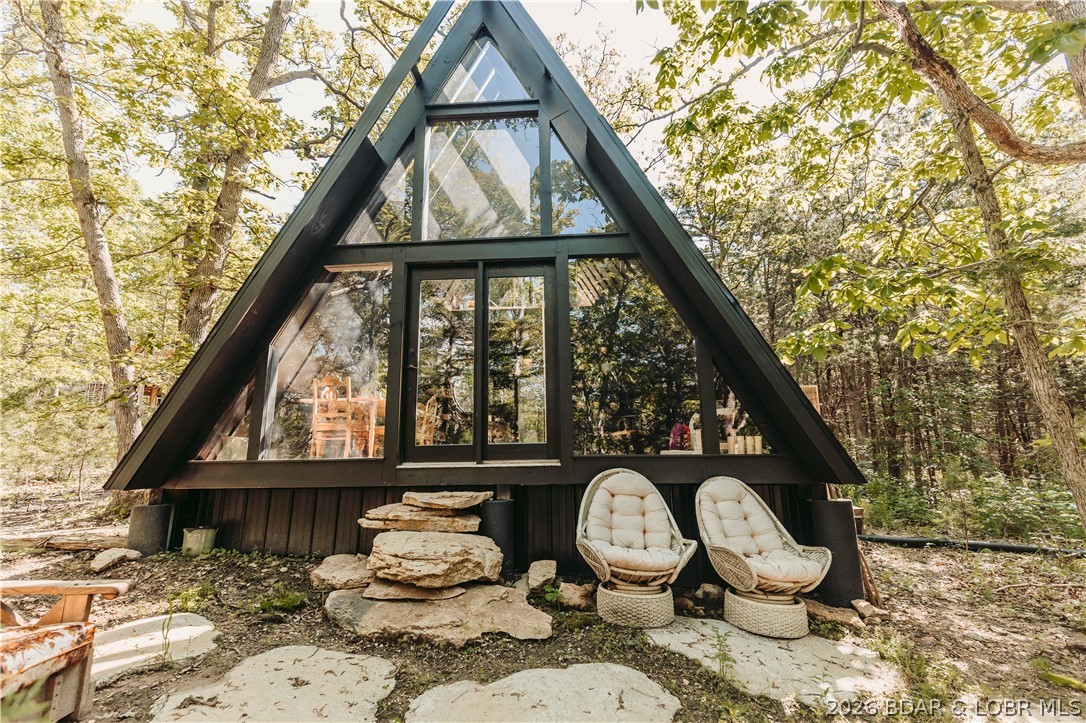 Endless possibilities await on this breathtaking 15-acre wooded retreat. Nestled among mature trees and accessed by a scenic circle drive, this one-of-a-kind property offers privacy, tranquility, and convenient access to the Lake of the Ozarks.
The custom A-frame guest home is truly special, featuring a stunning windows in the loft sleeping area, allowing you to fall asleep under the stars. You'll find an inviting foyer, open-concept living space, kitchenette, custom-tiled bathroom, large windows that showcase the surrounding natural beauty, and an outdoor entertaining area perfect for relaxing or hosting guests. A picturesque rock water feature adds to the peaceful atmosphere. With its unique design and setting, the guest home offers exciting potential for personal enjoyment or future rental opportunities. The three-story A-frame main home is ready for new owners to bring their vision to life and complete this dream property. Whether you're seeking a private residence, family retreat, vacation getaway, or investment opportunity, the possibilities are endless. Experience the beauty, serenity, and potential of this remarkable property.