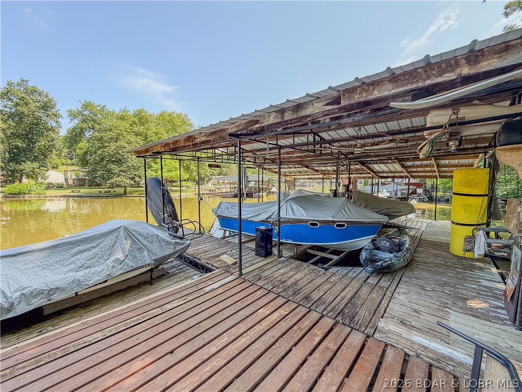 120 feet of lakefront, 2 slips with hoists, swim platform, and waver runner lift all in a peaceful setting and cove protected. Recent improvements include a roof approximately 3 years old, water heater only 1 year old, commercial grade vinyl flooring, 220V power outside, GFI protection at the house and dock, new bunks on both dock lifts, and a 14-foot electric awning over the deck. An oversized garage and carport add great storage for lake toys, vehicles, and weekend gear. Appliances and most furnishings stay, making this an easy place to start enjoying lake life right away. The walk to the dock does include several steps, but it is softened by mature trees, brick courtyard-style walkways, flowers, a pavilion and peaceful outdoor spaces that make the setting feel charming and secluded. Located close to marina, restaurant, and gas access. Come take a look and enjoy this summer at Lake of the Ozarks.