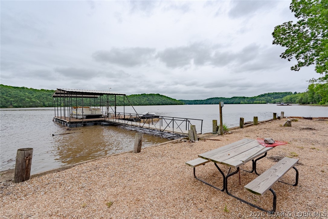Experience the ultimate Lake of the Ozarks lifestyle with this turnkey 4-bedroom, 2.5-bath lakefront retreat at the 66 MM! Boasting 150 ft of gentle shoreline and breathtaking main channel views, this fully furnished home is ready for you to start memory making from day one. The spacious lower level features a cozy wood-burning fireplace and walls of windows that bring the lake views inside. The kitchen offers abundant cabinet space, an easy-flow dining area, and beautiful lakefront scenery. The oversized remodeled primary ensuite is designed for comfort with a stunning walk-in shower, double sink vanity, and separate his-and-hers closets. Recent updates include modern Luxury Vinyl Plank flooring throughout the main floor. Outside, enjoy a large yard, a 20x24 two-car garage, and a dock with a 12x30 boat slip. A whole house Generac generator gives you peace of mind for the unexpected. Two additional lots across the road open the door for endless possibilities — build a shop, create extra parking, or design your own lake retreat expansion. To complete this incredible package, a 2008 22’ Party Barge pontoon in included. This is the total turnkey lake property you’ve been waiting for!