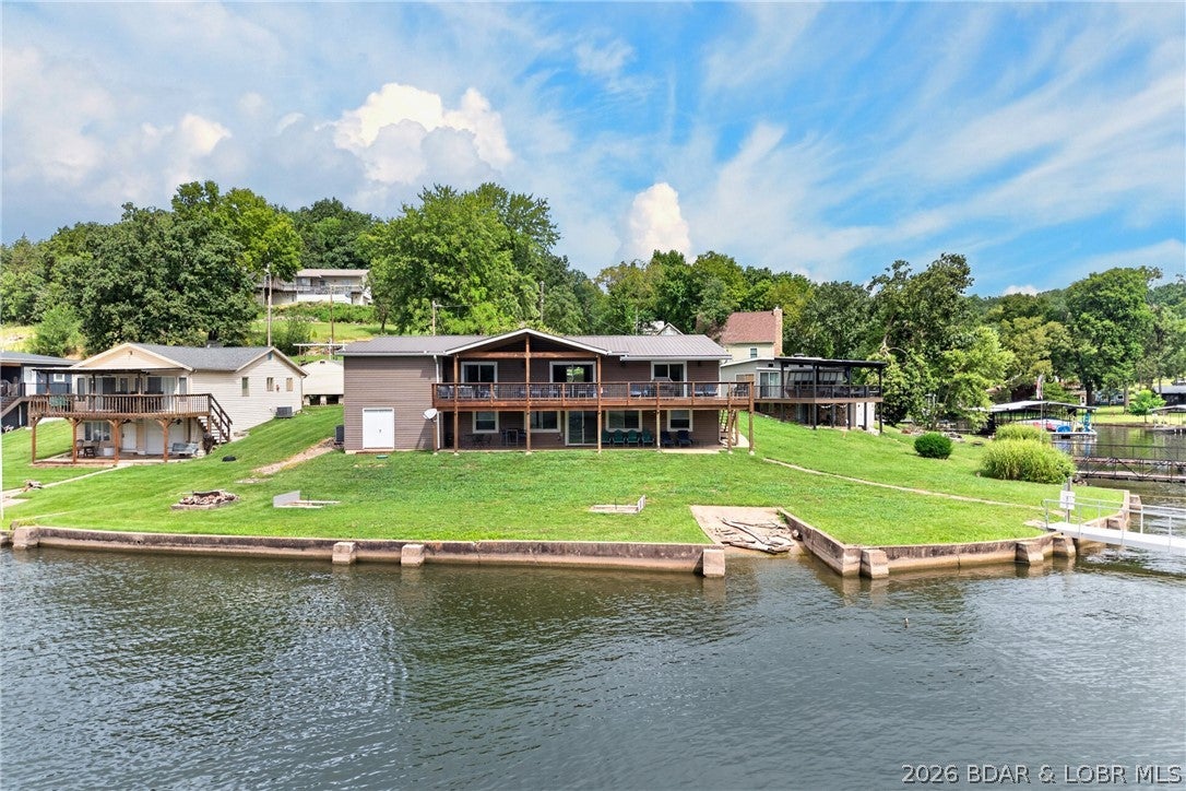 Wake up to Gravois Arm views from nearly every window in this 6-bedroom lakefront retreat. 166 feet of level shoreline turns the yard into your favorite gathering spot for bonfires, yard games, or just watching the water. Each level opens straight outside, so entertaining flows naturally from kitchen to patio to shoreline. The main-level primary suite pairs a lake view with a spacious private bath and attached laundry, plus two more bedrooms and a full bath round out the floor. Downstairs, a second family room with its own lake view centers around a wet bar opening to the patio, alongside three more bedrooms (non conforming) and a full bath with a walk-in shower and custom vessel-sink vanity. Granite counters and quality cabinetry carry throughout, and it's fully furnished. Six bedrooms split across two levels, each with its own living space and outdoor access, built for flexibility as a full-time residence or short-term rental with room for multiple groups. Outside, a two-well dock and private boat ramp make this one of the few move-in-ready waterfronts. One-car garage plus ample parking complete the package. 166 feet of level lake frontage at this price does not come up often.