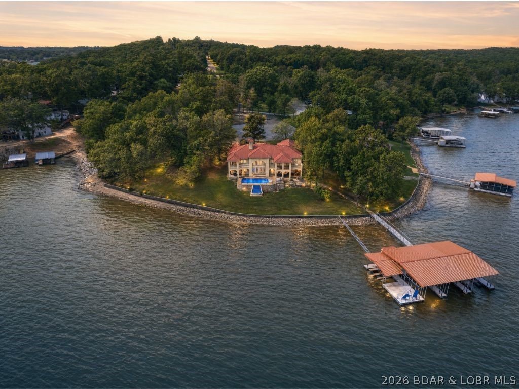 32 Quiet Waters sits on one of the flattest lots you’ll find at the Lake of the Ozarks & offering unmatched views of the Four Corners on a large lot with 242 feet of Lakefront. Recently remodeled in 2024, this turnkey lakefront retreat showcases quality throughout and features 8 bedrooms (including 2 non-conforming) and 6 full bathrooms with over 6000+ SF of living space—providing ample space to host and entertain large groups who may never want to leave. The walk-out lower level opens directly to your private in-ground pool, surrounded by outdoor entertaining space, creating the perfect setting to enjoy lake life to the fullest. By water, this property truly sits at the crossroads of the lake, allowing you to easily access all the best the Lake has to offer. The well-built concrete dock, featuring four slips, is conveniently accessed with just four steps from the home. The lower level is an entertainer’s dream, complete with a custom game room, full kitchen, & spacious family room. This is a rare opportunity to own a turnkey lakefront home built for fun, comfort, and unforgettable memories—on a lot that’s as flat as they come.