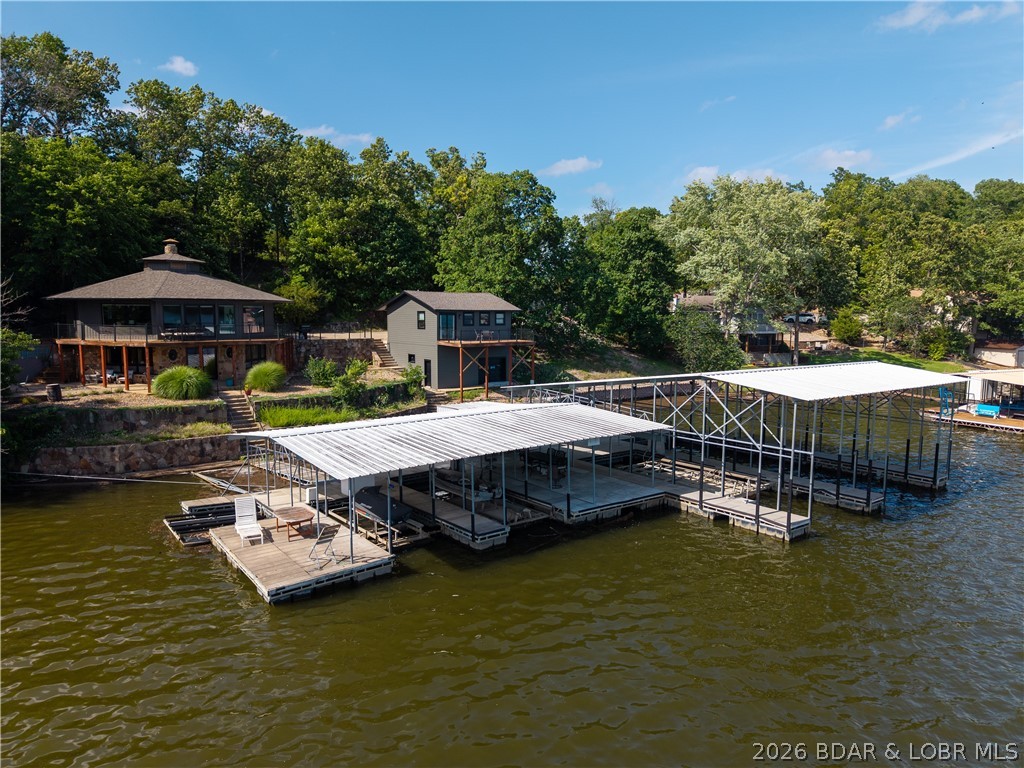 Escape to the quieter side of Lake of the Ozarks, where breathtaking views and effortless lake living come together in this beautifully updated waterfront retreat. The main home welcomes you with soaring wood ceilings, rich hardwood floors, a stunning stone fireplace, and an inviting open living space designed for relaxing and entertaining. The renovated kitchen features custom cabinetry and butcher block countertops, while the serene primary suite offers a spa-inspired bath with a soaking tub and walk-in tiled shower. A private 500 sq. ft. guest house with a full bath provides the perfect space for family and friends. Outside, enjoy expansive lakeside decks, covered and open patios, a hot tub, and a fire pit overlooking the water. The private dock offers four boat slips, dual PWC slips, and included hoists for effortless lake days. Tucked inside a peaceful cove with panoramic views, this proven income-producing property is the perfect full-time residence, luxury getaway, or exceptional investment opportunity where every day feels like a vacation.