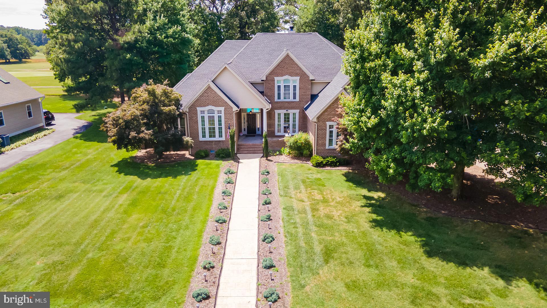 Nestled on a beautifully landscaped 0.61-acre lot overlooking the Nutters Crossing Golf Course, this stately residence combines timeless elegance with exceptional indoor and outdoor living. A grand foyer welcomes you and is flanked by a formal dining room and a distinguished library featuring French doors, built-in shelving, and rich wood flooring. Straight ahead, the sunken living room serves as a stunning centerpiece with a gas fireplace and a dramatic curved wall of windows that frame picturesque views of the private pool and backyard oasis. Designed for both everyday living and entertaining, the spacious kitchen offers abundant cabinetry, a gas cooktop, double wall ovens, a center island with counter seating and pendant lighting, and a bright breakfast nook. The kitchen flows seamlessly into the family room, creating an inviting gathering space. A convenient powder room and main-level laundry room add to the home's functionality. The main-level primary suite provides a luxurious retreat, complete with two walk-in closets and a private sitting room or library featuring French doors, built-in shelving, and a fireplace. The ensuite bath is thoughtfully appointed with a jetted soaking tub, dual vanities, a step-in shower, private water closet, and abundant natural light. Upstairs, three generously sized bedrooms and two full bathrooms provide comfortable accommodations for family and guests. Car enthusiasts and hobbyists will appreciate the oversized four-car garage with two separate entrances, each accommodating two vehicles. Outside, the manicured grounds showcase carefully designed landscaping surrounding the covered front entrance, while the fenced backyard is an entertainer's dream. Extensive hardscaping surrounds the private pool, complemented by colorful flower beds and ample space for large gatherings, outdoor dining, and recreation. Residents of Nutters Crossing enjoy access to a substantial clubhouse and an acclaimed golf course, all within an established neighborhood setting just east of downtown Salisbury. Offering a peaceful, pastoral atmosphere with convenient access to local amenities, this exceptional property presents a rare opportunity to enjoy refined living in one of the area's most desirable communities.
