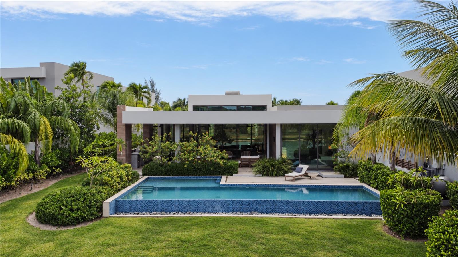 5 Salt Lane is located in “The Estates” section of The Isles at Dorado Beach, known for its larger lots and floorplans, greater privacy, phenomenal water views and a consistent breeze. As you enter the property, there is an immediate sense of space. Nearly 15-foot ceilings give the main living space a wonderful sense of volume, while the single-level layout creates an easy, natural flow from one room to the next. The living and dining areas flow into the kitchen, and an entire wall of glass doors disappears into the walls, allowing the expansive living area to open completely toward the pool and the landscape beyond.  The bedrooms are spread throughout the home, creating little pockets of privacy and making the house feel much more intimate. The primary suite opens directly to the outdoors, creating a private connection to the pool. Its bathroom feels like a private retreat, with a freestanding tub, four showerheads, double vanities, walk-in closet, and a double outdoor shower tucked away in complete privacy.
But it is the backyard that sets this home apart.  The pool seems to disappear into the landscape, and the lake begins just beyond the lawn. There are no homes directly behind you, just water, mountains, open space and sky. The prevailing breeze moves in from the east, and with nothing blocking the property’s exposure, it finds its way through the outdoor spaces throughout the day.
This is a house made for living outside. Long lunches become afternoon swims. Evenings naturally move toward the outdoor kitchen and pool. And then, as the sun begins to set, everything changes. The sky turns shades of pink and orange, the light softens, and the house takes on an entirely different feeling, a feeling that you have arrived somewhere truly special. And those are the moments that are priceless. 
Built in 2022 with four ensuite bedrooms, a heated saltwater infinity-edge pool, outdoor kitchen, full backup generator, 900-gallon water cistern, water softener system, solar water heater and two-car garage with golf cart space and a Tesla charger, the home offers every modern convenience.  Beautifully furnished and offered with furniture negotiable.