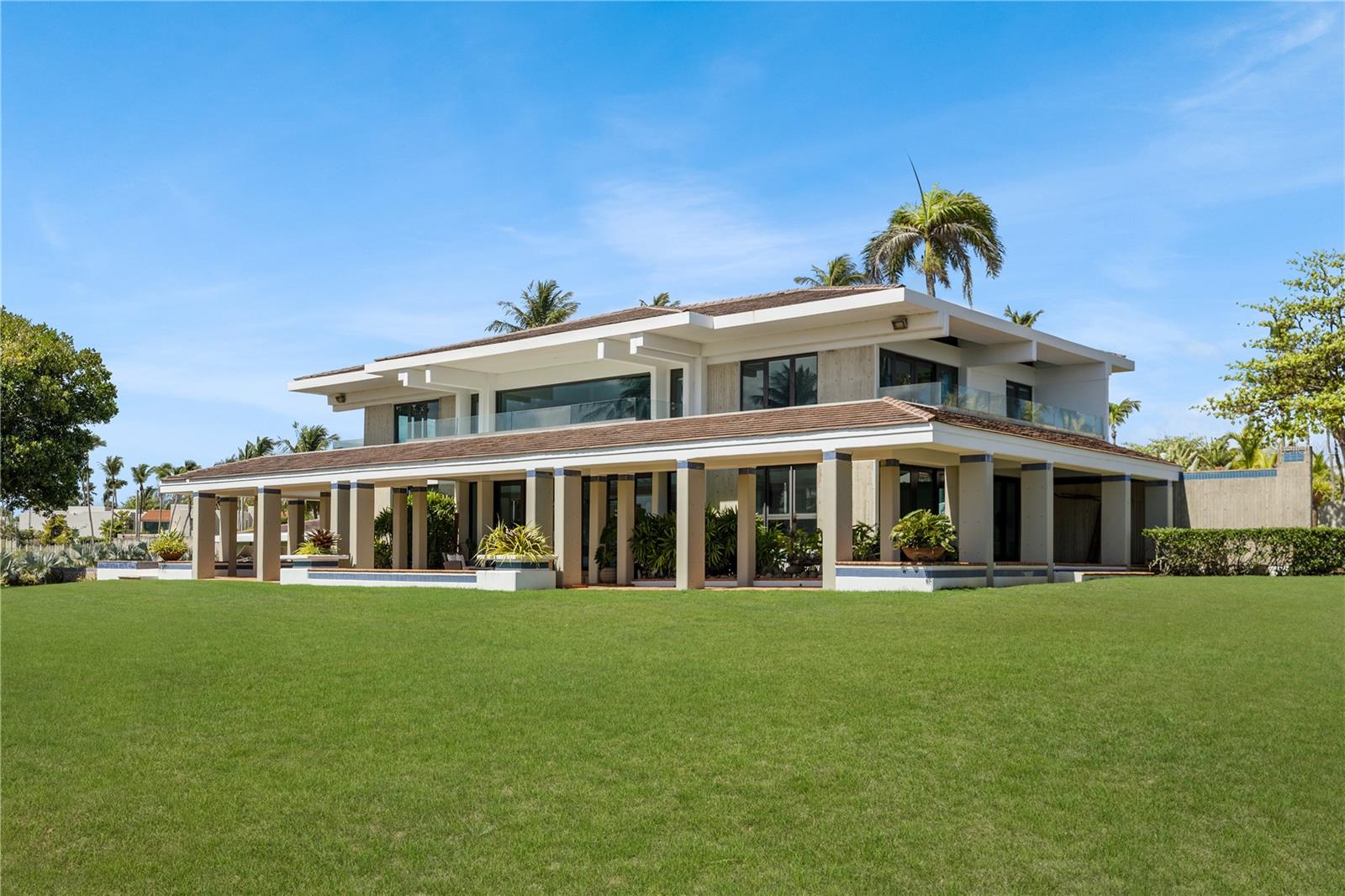 Introducing The Redonda Estate. A remarkable private residence set on more than three acres overlooking the Mata Redonda Lagoon and the West Golf Course of Dorado Beach Resort. Defined by its scale, privacy, and privileged setting, the property features a private pond, proximity to the beach, and extensive grounds that create a remarkable feeling of privacy and openness within one of Dorado’s most coveted residential enclaves. Designed as a private retreat yet equally suited to grand-scale entertaining, the property encompasses a turn-key main residence of more than 9,000 square feet, including 4,865 square feet of interior living space, complemented by a separate 1,635-square-foot guest house. Beyond its existing residences, the extraordinary acreage and Residential-Touristic zoning create an uncommon range of possibilities – from a multigenerational family compound or the addition of further residential components to the creation of a private resort-like environment with recreational courts, gardens, and expansive outdoor amenities. Originally designed by Thomas S. Marvel, known for championing tropical modernism in Puerto Rico and the Caribbean, The Redonda Estate was completely renovated in 2016. The main residence balances contemporary refinement with an effortless, highly livable design. Interiors open naturally to the surrounding terraces and gardens, allowing the beauty of the lagoon, golf course, and tropical landscape to become part of everyday life. The chef’s kitchen features custom Cucine Lube Italian cabinetry, elegant quartz countertops, a generous central island designed for gathering, and a beautifully appointed butler’s pantry. Multiple living and entertaining spaces, including two living rooms and a separate family room, provide flexibility for both intimate moments and larger gatherings. The main residence offers four bedrooms plus a guest suite, four full bathrooms, and a half bathroom. The primary suite is conceived as a private sanctuary, opening onto a generous terrace overlooking the lagoon and golf course. Its generous primary bath features a walk-in shower and spa-inspired finishes. Outdoor living is central to the experience. Approximately 4,475 square feet of covered and uncovered terraces, balconies, and decks extend the living spaces into the landscape, creating distinct settings for dining, lounging, entertaining, and simply taking in the panoramic surroundings. The infinity-edge pool, meticulously landscaped gardens, and sprawling lawns complete the setting, creating an atmosphere of privacy and tranquility.
The separate guest house provides two guest rooms, one full bathroom and a half bathroom, together with a two-car garage, mechanical rooms, and additional storage, offering privacy and independence for extended family, guests, or staff. Electrolux and BOSCH premium appliances, refined finishes, a water cistern, diesel backup generator, and meticulous attention to detail further enhance the property’s functionality and resilience. Rarely does an estate of this scale, versatility, and distinction become available in Dorado. With more than three acres, a private pond, commanding lagoon and golf course views, and proximity to the beach, this is not simply a home – it is an exceptional legacy property and a truly extraordinary private estate.