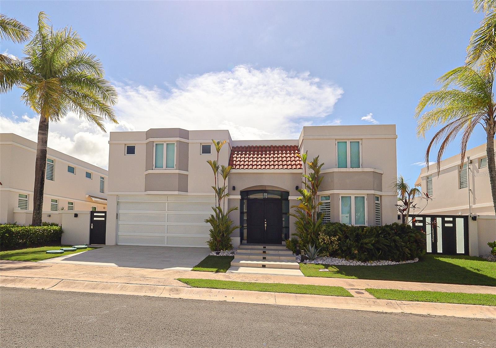 Welcome to this move-in-ready residence in Paseo Los Corales I, one of Dorado’s most desirable gated communities. Set on a spacious 580-square-meter lot, the home offers approximately 4,300 square feet of construction with four bedrooms, a private office, two full bathrooms, two half bathrooms, open-concept living, dining, and family areas, a covered terrace, one laundry room, and a two-car garage. The expansive primary suite features a generous walk-in closet with a built-in closet system, and an oversized private bathroom with a soaking tub, walk-in shower, enclosed toilet and bidet room, and large double-sink vanity.
The residence has been thoughtfully updated with more than $230,000 in improvements, blending refined interiors with resort-style outdoor living. At the heart of the home is a beautifully remodeled open kitchen featuring new custom cabinetry, waterfall-edge countertops, custom shelving, a new sink and faucet, disposal, cooktop, microwave, and oven. Additional interior updates include fresh Sherwin-Williams paint throughout, a statement entry chandelier, and a newly installed sliding glass door creating a seamless connection to the backyard. Other significant upgrades include four new air-conditioning units, extensive concrete roof repairs and waterproofing, a custom perforated-aluminum garage door with LiftMaster opener, custom aluminum side gates, and new tile throughout the driveway, garage, front walkway, and front patio.
Designed for entertaining and relaxation, the transformed backyard features new patio tile, professionally installed turf with a custom putting green, and an extended concrete pad with a basketball hoop and custom sport-court flooring. The outdoor space also includes a fully renovated bathroom and a custom bar with lighting, a sink, and an under-counter refrigerator. Additional enhancements include dedicated electrical connections for a cold plunge and sauna, upgraded outdoor lighting, refreshed landscaping, a 500-gallon water cistern, a solar water heater, and a 14 kVA gas-powered backup generator with a 250-pound gas tank.
Residents of Paseo Los Corales I enjoy access to a swimming pool, tennis court, gym, gazebo, and 24-hour security. The community is conveniently located near Dorado’s beaches, private schools, restaurants, shops, pharmacies, entertainment, and new hospital.