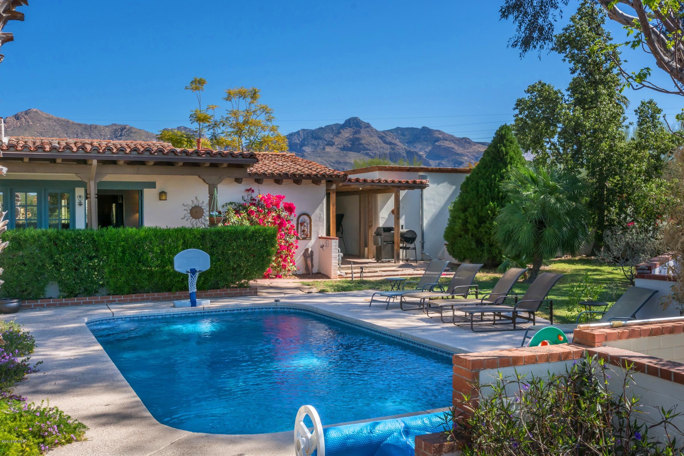 This gorgeous southwest adobe home w/lovely mountain views boasts all the style, charm & amenities you'd expect to pay so much more for.  From the exposed wood beam ceilings, gorgeous scored concrete floors, 2 fabulous fireplaces, stunningly remodeled kitchen w/hickory cabs, SS appl, honed slate counters & designer tile backsplashes to the luxurious Mstr Ste w/soaking bear claw tub, sep shower, vessel sink, walk-in closet & French doors leading out to private patio & hot tub.  Other features incl lush entertainer's backyard w/refreshing pool, huge patio, lots of hardscape & very cool BBQ/FP surrounded by cozy banco seating. 2-car gar, 2-car carport, tons of storage, circular concrete driveway & private gated entrance. With all it's classic Tucson character, this home is truly irresistible!