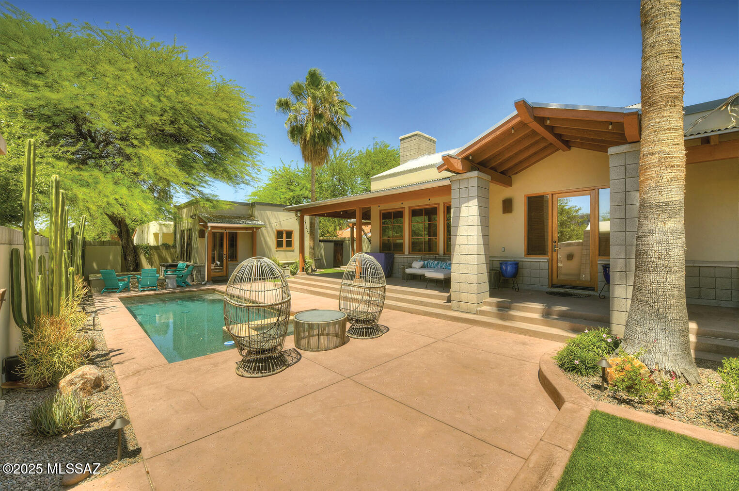 Truly one-of-a-kind contemporary home, built in 2001, nestled in the historic Arizona Inn neighborhood—just one block east of Banner University Hospital.  Crafted with exceptional quality and meticulous attention to detail, this private, fully walled midtown sanctuary invites you in through a charming, gated entrance. Enjoy wraparound porches, a sparkling pool and hot tub, a 2,038 sq. ft. main residence with 3 bedrooms, and a 362 sq. ft. guest house your visitors may never want to leave.  Step inside the main home to soaring cathedral ceilings with exposed beams, a cozy fireplace, and stunning African teak wood flooring. The gourmet kitchen is a chef's dream—featuring granite countertops, stainless steel appliances, a center island with breakfast bar, scored & colored concrete flooring, and custom cherry wood cabinetry.  Additional highlights include wood-framed windows with custom coverings, and a guest house equipped with a new mini-split HVAC system, ideal for comfort and privacy.  Enjoy the ease of modern living with recent Smart Home upgrades including a Ring security system, Nest thermostat, Yale Smart lock, Chamberlain myQ Smart Garage control, and Pentair remote pool/spa operation. The home also features a Sonos indoor/outdoor whole-house audio system and a Tesla wall charger in the garage.  Live just steps from the Arizona Inn, and minutes to the U of A, shopping, dining, and entertainment.  If you're looking for quality, charm, and unbeatable location, this home is a rare gem. Ask about the option to purchase furnishings via separate bill of sale.