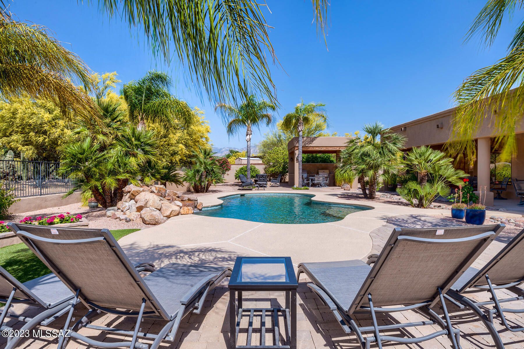 Spacious home with resort-style back yard -- perfect for entertaining -- in a small, quiet neighborhood nestled between Oro Valley and Marana. A circular drive takes you to arched iron entrance doors leading into the foyer with soaring ceilings and looking straight through to the back yard with its pool, rock waterfall, mature palm and citrus trees; ramada with two barbecues; numerous sitting areas and cottage-style shed. Just inside the foyer is a large office with 8' double doors and the dining and living room areas. Continue on through the open floor plan with arched windows and skylights throughout which make the home light and bright. Huge primary bedroom suite. Large usable area behind fenced-in yard currently serves as a natural buffer. Large 3-car garage with built-ins. Owner/Agent