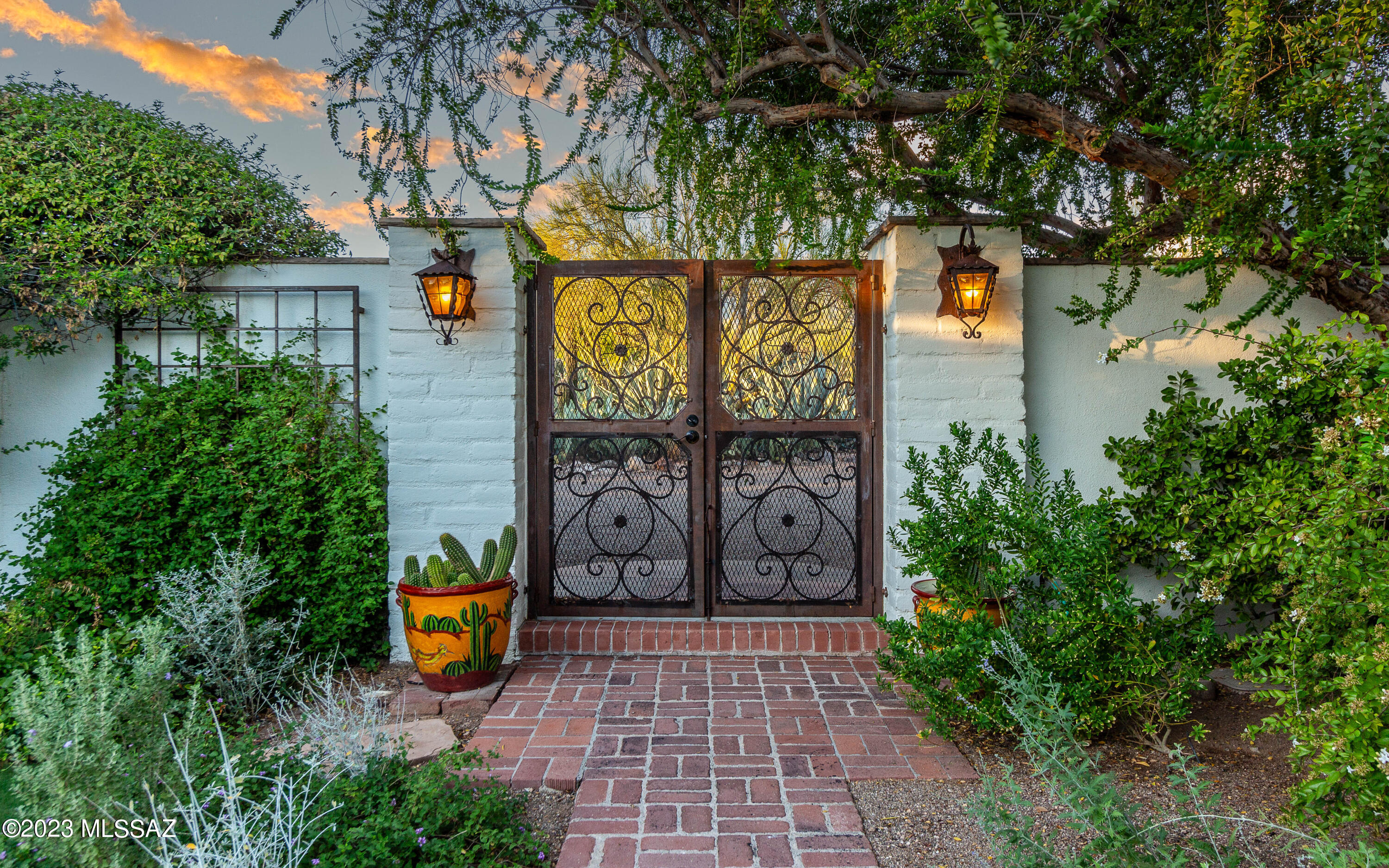 See why this charming historic home in the heart of Tucson's Catalina Foothills Estates won the Tucson Realtor Home Tour. Designed by renowned architect Josias Joesler in the late 1930s, this adobe house on over two acres features beamed ceilings, carved doors, lintel beamed doorways, bookcases built into the 18'' adobe walls, hand-forged iron gates, and a private walled courtyard. The living room has twelve-foot viga beamed ceilings, a wood burning fireplace and exceptional picture windows. The kitchen has been updated with Carrera marble countertops and Viking appliances. The fully windowed dining room has French doors leading to the covered patio overlooking the pool. The primary bedroom suite offers furniture-style built-in closets, large windows, and a private patio. The second bedroom, or guest suite has a sitting area, fireplace, ramada covered patio and French doors with private access to the courtyard. Along with three beautiful bedrooms, there is a large library, separate office and family room. Built around a walled courtyard, this U-shaped design creates areas of privacy and quiet throughout the house. The home retains a high level of seclusion, and exceptional rural character yet is only minutes from the shopping and dining experiences at La Encantada, Joesler Village
and St. Philips Plaza.