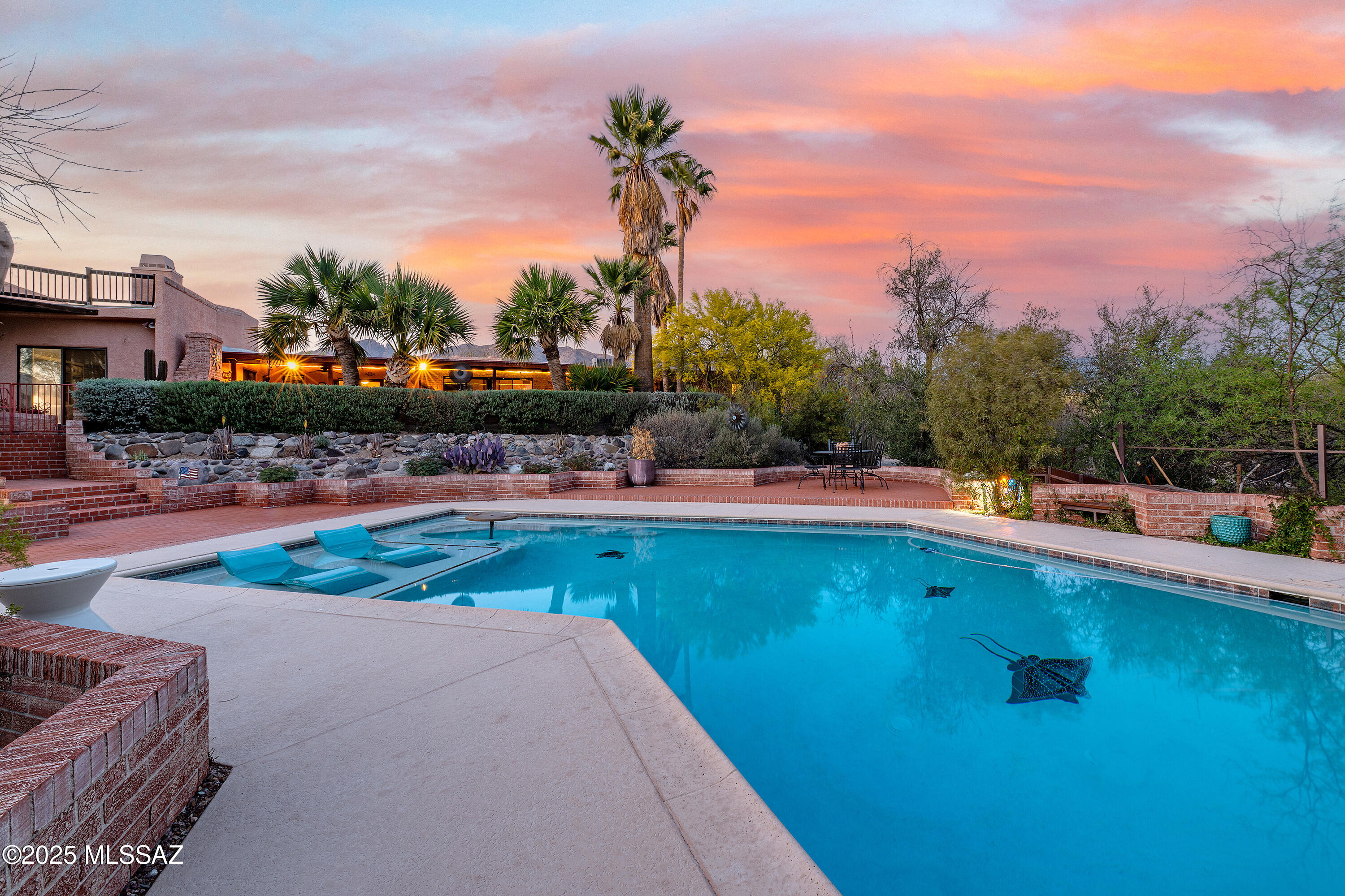Nestled on over an acre of pristine desert landscape, this meticulously built masonry home blends privacy, comfort, and timeless Southwest charm. Tucked away in the sought-after Flecha Caida neighborhood—within the Catalina Foothills School District 16—this residence is thoughtfully set far back from the road, offering a serene and secluded retreat.
The main house features three spacious bedrooms and two bathrooms. At its heart, the living and family rooms share a dramatic double-sided brick fireplace, infusing the space with warmth and character.
Adding to the property's appeal is a charming guest house, complete with one bedroom, one bathroom and a cozy fireplace, perfect for visitors or extended family. Step outside to your own private oasis: a multi-level brick patio with a built outdoor fireplace invites relaxed evenings under the stars, while the sparkling pool - accented with custom mosaic tile art - provides a striking centerpiece and a refreshing escape.
The expansive lot also offers ample space for RV parking or future enhancements, giving you the flexibility to tailor the property to your unique vision.
Whether you're seeking a tranquil desert sanctuary, an entertainer's dream, or a home with versatile living options, this exceptional property offers it all - ideally situated in one of Tucson's most desirable locations.