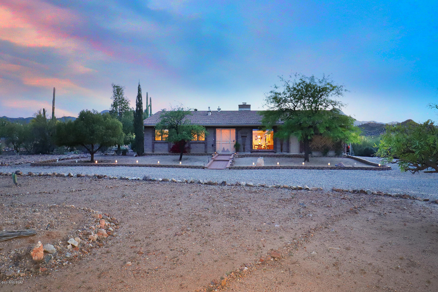 Welcome to the wide open spaces of West Tucson, where the views are wrap-around, the stars are bright and the only sounds are breezes and birds. Enjoy seeing Orion and the Big Dipper so clearly you feel as if you could touch them. There's a delightful, impeccably-maintained and very livable home attached to this lifestyle that's now available for the first time in over 30 years. It's set in a cul-de-sac on 1 ½ Acres, with a large circular driveway, mature landscaping and a welcoming brick walkway to the entry. The rooms are spacious, most have hard surface floors and all enjoy marvelous views of the Catalina or Tucson Mountains. A screened entry leads to the large living room graced with high vaulted ceilings accented with dark wood beams and a fireplace set in stone surround and hearth that has been retrofitted with a Wells Fireplace insert that provides auxiliary heat to the home. A raised dining area, also with beamed ceiling, is adjacent. The family room and kitchen are comfortable spaces, with the family room enjoying a cute little wet bar with a "belly up to the bar" counter for barstools. The kitchen has gorgeous custom hickory cabinets outfitted with pull-out drawers for easy access to stored items. The huge and fully enclosed rear yard provides a broad and deep covered terrace from which to enjoy views of the sun and moon setting over the Tucson Mountains, depending upon time of day. (Please see photo of moon setting over nearby hill taken by owner.) There's a large Pebble Tec pool that the owners report has been much enjoyed by grandchildren and themselves that includes a lounging area, a wood-burning adobe fireplace to gather around, and a ramada with an outdoor grill and bar seating area. The yard is fully enclosed by a handsome pueblo brick wall, and includes more of the attractive red bricks found in the front walkway. 
The master bedroom is spacious, with sliding glass doors out to the fabulous rear yard. Included is a sitting area, two walk-in closets and another large mirrored sliding door closet. Along woth a bath area that includes a shower. Two additional bedrooms enjoy several additional closets, with an attractive nearby full bath. The "piece de la resistance of this home, for car lovers, are the garage with space for four vehicles, the carport accommodating two additional vehicles, and another separate garage shed, plus room to work on them if desired. Not to forget the two large sheds on the property, that can be for garden or storage items and will keep everything dry. 
This is a very comfortable home, with room for everyone, whether for family, entertaining or equally easy to just put your feet up and enjoy. There is easy access to the new Tucson Outlet Mall, grocery stores, restaurants in the area and downtown as well, and medical facilities including Northwest Medical Center, St. Mary's Hospital and an urgent care center. Neighbors are quiet and friendly, and it's a safe and easy area. You are invited to view this delightful and move-in-ready home at your earliest convenience.
