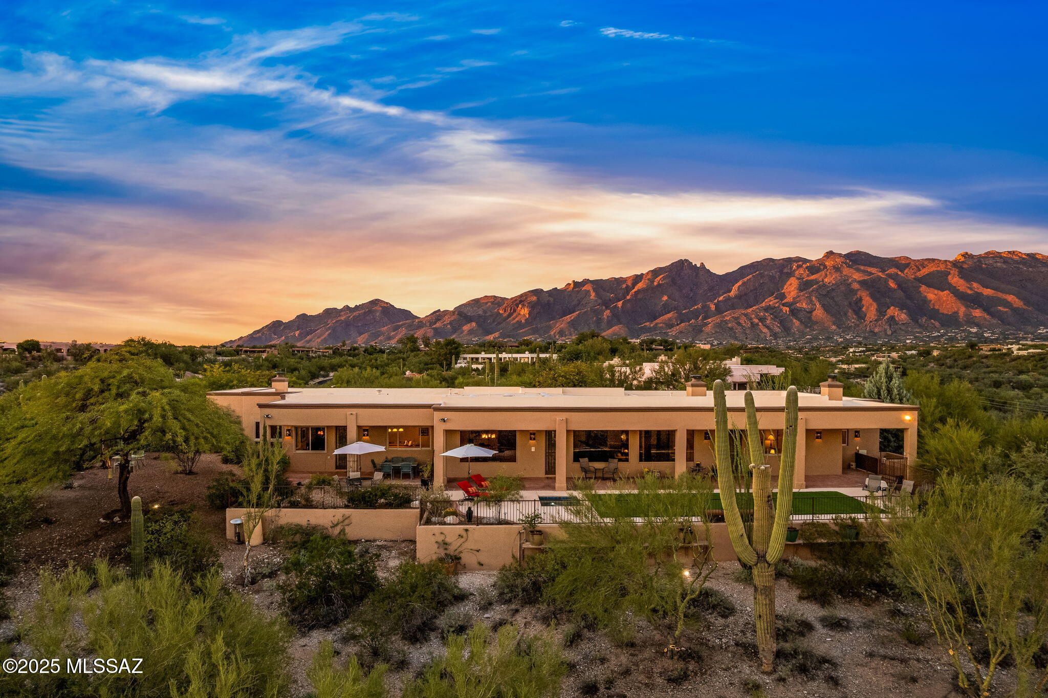 Perched high on a private ridgetop lot  overlooking the sparkling lights of Tucson, this timeless desert contemporary home embodies the sought after Tucson Foothills lifestyle. Located in one of Tucson's most prestigious and secure gated communities - Catalina Foothills Estates #10 (CAT 10), revered by locals for its two manned security gates, unbeatable location, and unmatched prestige, CAT 10 offers exclusivity and convenience just minutes from La Paloma Country Club (5 minutes) and The University of Arizona (15 minutes). Nestled at the end of a quiet cul-de-sac, this home sits on a 2.28-acre lot, offering exceptional privacy, views and tranquility. A long, private driveway leads to a rare oversized 4-car garage. Upon entering, expansive picture windows frame the sweeping city lights and mountain views, seamlessly blending indoor comfort with the desirable outdoor Tucson lifestyle. Perfect as a luxurious year-round residence or a sun-soaked winter retreat, the outdoor spaces feature a spa, expansive front and rear covered brick patios, and lush green lawn-ideal for enjoying Tucson's year-round outdoor lifestyle. The recently renovated kitchen is both functional and beautiful, showcasing two-tone custom cabinetry, granite and mesquite countertops, a walk-in pantry, stainless appliances and commanding views from the kitchen sink. The Primary Suite is a true sanctuary, highlighted by a gas fireplace, built-in bookcases, and unforgettable city views. The spa like primary bathroom includes a walk-in shower, soaking tub, dual water closets, and authentic hand-painted Talavera tile and a spacious walk in closet. A split floor plan provides privacy for all, featuring four en-suite bedrooms plus a den/5th bedroom with built-in shelving & 1/2 bath. Throughout the home, stunning Mexican tile and mesquite wood flooring flow seamlessly without a single step, enhancing the homes accessibility. This timeless Tucson home masterfully combines luxury, understated elegance, views, total privacy, and retains its Southwest charm-a rare offering in on of Tucson's most sought-after gated foothills community. Whether you're seeking a year-round residence or an elegant winter retreat, this home offers the perfect balance of luxury & comfort, in a beautiful natural setting offering total peace and tranquility. Discover why discerning buyers from across the country are choosing the Catalina Foothills-you will be hard pressed to find a better place to call home!