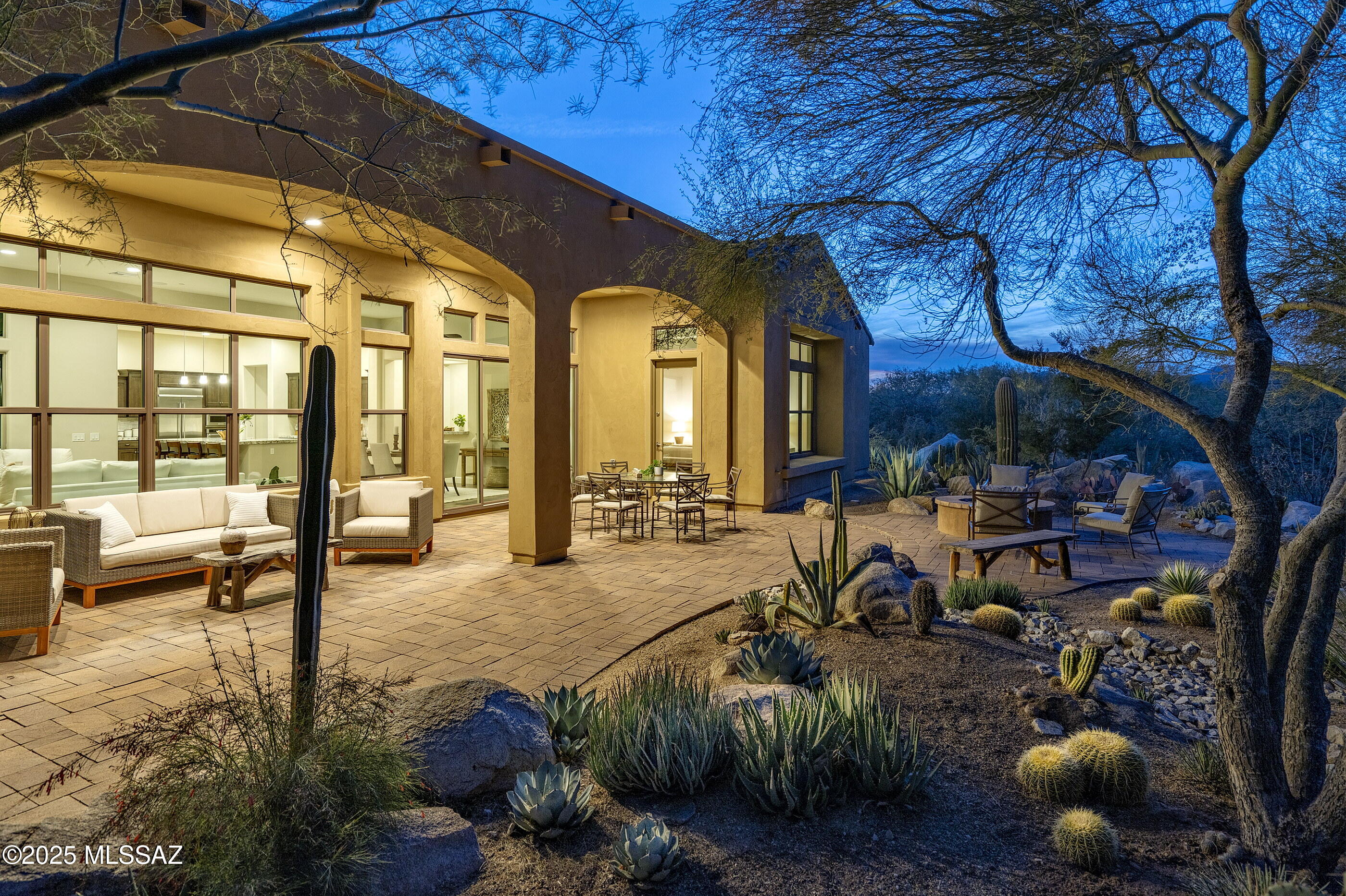 Located behind the gates of the exclusive Stone Canyon community and situated in the shadow of the Tortolita Mountains, this private golf community spans over 1,400 acres of untouched desert terrain, where the stark beauty of the rugged topography meets the architecture of quiet refinement. As one steps inside this residence, the living areas reveal themselves as a celebration of space, with expansive glass walls that dissolve the barrier between inside and out, framing views of the desert landscape as if it were a painting on display. 

The interior spaces are conceived as a sequence of rooms that flow effortlessly, while maintaining a distinct purpose. Natural light is paramount, with high North facing clerestory windows and sliding glass doors that open onto shaded patios. Overhanging patios extend casting deep, dynamic shadows that shift with the sun, an homage to the ever-changing light of the Sonoran Desert with tall slender cacti punctuating the space like organic sculptures, their forms complementing the rectilinear lines of the architecture.

The kitchen is a meticulously composed space, where architectural proportions and materiality converge to create an atmosphere of restrained elegance. Custom wood-toned cabinetry offers a seamless storage solution, its natural finish introducing warmth while maintaining a sense of continuity with the surrounding design. Stainless steel appliances are recessed and flush-mounted, complemented by granite countertops, providing a tactile contrast to the cabinetry's more organic texture. Anchored by a central island and framed by expansive high ceilings, the space overlooks a garden courtyard allowing natural light to permeate and enhance the interplay between interior and exterior.

The primary bedroom serves as a quiet retreat, with large picture windows framing curated views of the landscape, drawing the outdoors inward. The space transitions seamlessly into the adjoining primary bathroom, where dual vanities with black quartz countertops, anchor the design in simplicity and material integrity. A walk-in shower, enclosed in frameless glass, flanked by a large soaking tub positioned to balance functionality with moments of quiet repose. Completing the suite, a generously scaled walk-in dressing closet is outfitted with custom millwork, ensuring optimal storage.

The verdant garden is the final, essential element of the home, a deliberate blending of design and desert ecology. Embracing the Sonoran Desert's inherent beauty, with an arrangement of saguaros, ocotillos, and golden barrel cacti in patterns that echo the rhythm of the natural surroundings. Low-lying agaves with their radial symmetry create focal points, while gravel paths meander through the space, inviting exploration without disrupting the natural flow. Small pockets of wildflowersdesert marigolds, penstemonsadd bursts of color, drawing the eye to unexpected corners. The garden is not just a backdrop but an integral part of the living experience, embodying the unity of form, function, and the organic environment.