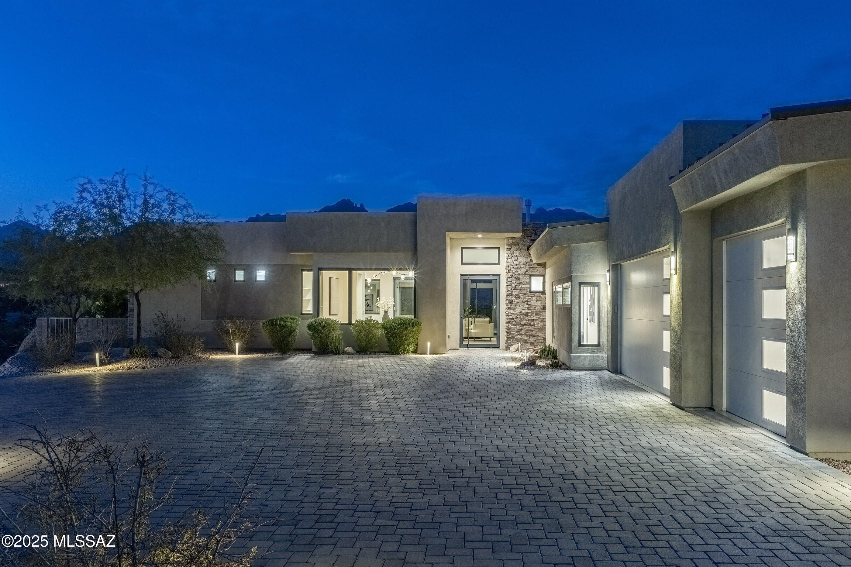 Stretching boldly across one of the largest lots in the prestigious, guard-gated Catalina Foothills 10 community, this commanding contemporary residence is sited on 3.22 acres. A long, meandering cobblestone driveway winds elegantly through the landscape, guiding you to this hilltop residence, where architecture and nature converge in harmony. From this vantage point, sweeping vistas unfold in both directions, with Catalina Mountain views to the north and panoramic city views to the south, creating a living environment that celebrates the beauty of both desert and skyline. The arrival sequence of this striking home establishes a powerful visual dialogue, juxtaposing the clean, sculptural lines of the architecture against the natural contours of the land. The stucco clad exterior asserts a contemporary statement across two central view corridors. Just off the motor court, a large oversized three-car garage offers both convenience and seamless integration into the property's design.

Entry is made through a dramatic full glass pivot door, immediately revealing the great room, where natural light pours through floor-to-ceiling retractable glass walls. The space flows effortlessly onto the rear veranda, framing breathtaking views and providing an ideal vantage point for both quiet mornings and evening entertainment. As the sun rises, soft light illuminates the warm tile floors and rich textures of the interior, while at twilight, the city lights shimmer below. 

The kitchen is a masterclass in refined design and functional clarity. Rich dark wood flat-panel cabinetry is paired with stainless steel appliances and carefully detailed hardware, creating a space that is both composed and highly practical. Thoughtfully arranged for effortless flow, the kitchen guides movement naturally through work and gathering areas, making it as inviting for intimate meals as it is for larger-scale entertaining. The adjacent dining room and breakfast nook are accented with modern linear globe chandelier ceiling fixtures, offering subtle, elegant illumination that enhances the ambiance of these spaces. Expansive tile floors extend throughout the home, providing continuity and a sophisticated, understated foundation for both living and leisure.

The residence is organized around a thoughtful split-bedroom layout, emphasizing privacy and function. The owner's suite is positioned on the northwest end of the home, oriented to capture Catalina Mountain views. The suite incorporates a primary bathroom with clean lines and refined finishes, along with a walk-in dressing suite designed for both capacity and organization. Three secondary bedrooms are located on the east end, each generously scaled with ample closet storage, providing well-resolved accommodations for family or guests.

The site was carefully designed to preserve a generous expanse of level ground for outdoor living. Expansive covered verandas extend the interior spaces, creating a seamless connection between indoors and out. The rear yard features a fully integrated pool positioned to maximize Catalina Mountain view corridors, complemented by a built-in barbecue and ample seating beneath the covered patios. Integrated low-voltage landscape lighting highlights key architectural and landscape features, while a professionally installed irrigation system supports the home's carefully planned plantings. Together, these elements create outdoor spaces that are both visually commanding and effortlessly functionalideal for entertaining or relaxation.