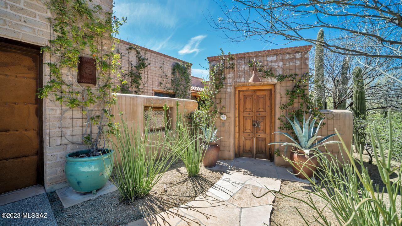 Authentic Stellar-Gray adobe home in gated Sky Ranch on almost 1/2 acre! Unique to the Northwest part of town & surrounded by 100's of acres of protected natural open space. Incredible Catalina views from the private backyard patio w/ FRPL ! Antique doors open to walled CTYD w/ lovely plantings & fountain. Iron/glass front door opens to great room w/ FRPL accented w/Cantera Stone, Concrete floors & 16'' mud-adobe walls. Viga beamed ceilings, knotty alder cabinets w/ rough edge Quartsite Taj Mahal throughout home. All Viking appliances incl 6 burner gas range, butcher block island. This split plan offers incredible designer nuances that one needs to see to appreciate. Come view the higher standards of construction w/ all the southwest Tucsonian charm in this sought after community!