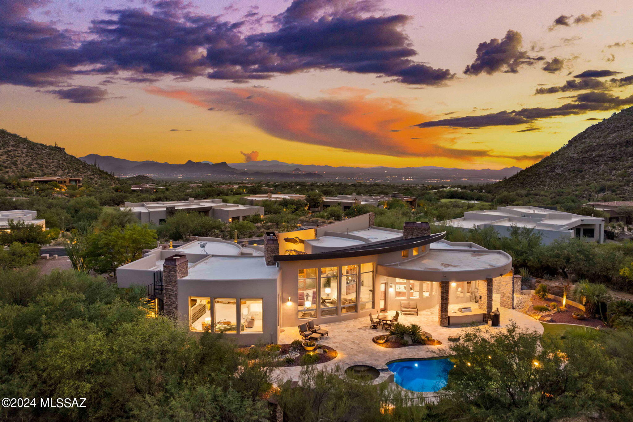 Nestled on the prestigious 5th Fairway of the Gallery North Course, this stunning custom home offers a perfect blend of luxury and nature. Thoughtfully crafted with fine appointments and modern architectural design, the property features curved walls, intricate ceiling details, and walls of windows that create a profound sense of grandeur. Upon arrival, you'll be greeted by a welcoming courtyard in a prestigious private guard-gated community, tucked into the high Canyon walls of Canyon Pass on a sprawling 0.75-acre lot. The interior design by Liz Ryan adds a touch of sophistication to every room. Conveniently located just 45 minutes from Tucson airport and 90 minutes from Phoenix airport, this home is easily accessible yet feels miles away from the hustle and bustle. Surrounded by breathtaking mountain beauty, including saguaros and natural desert vegetation, this home boasts an open split floor plan with soaring high ceilings and a massive fireplace with a temperature sensor. Floor-to-ceiling windows frame the majestic Tortolita mountains, flooding the home with natural light. The property includes four ensuite bedrooms, including two primary suites, each with private patios, ensuring comfort and privacy for all residents. The formal dining area and stone flooring throughout the home, complemented by carpeted bedrooms, add to the home's elegance. The gourmet kitchen is a chef's dream with a massive Cambria Britannica island, designer stainless steel appliances, including a Miele auto coffee machine, Sub-Zero refrigerator, 6-burner 48" Monogram range with griddle and downdraft, Sub-Zero two-drawer cabinet refrigerator, Bosch dishwasher, and an AquaSential reverse osmosis tankless drinking water system. Custom cabinetry offers ample storage space and spectacular views from every angle.
The backyard oasis is an entertainer's paradise, featuring travertine flooring, a built-in BBQ with a sink, mini fridge, and bar stool seating. Enjoy evenings by the fire pit or practice your short game on the putting green. A spiral staircase leads to the rooftop deck, providing panoramic mountain views, city lights, the golf course, and breathtaking sunsets. The heated PebbleTec pool and spa offer a spacious and relaxing retreat, allowing you to absorb the incredible views in complete serenity. This remarkable property truly embodies luxury living in a serene desert landscape.