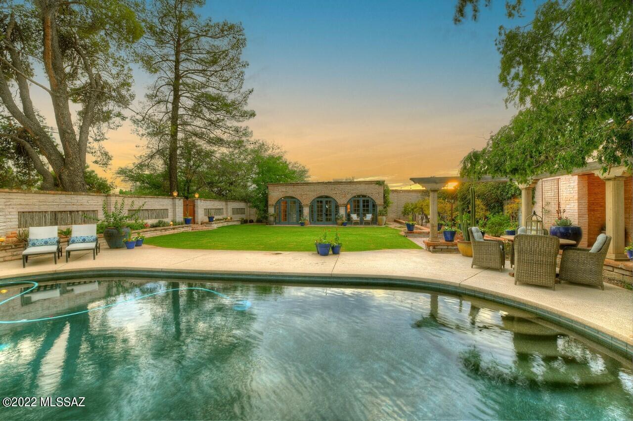 Like so many beautiful homes, the story begins as you enter hand forged iron gates. A gracious compound with a classic adobe home, a guest casita with wall of french doors,  columned terrace, pool, and all  nestled around green grass, magnificent trees, and splashes of flowers. It is a magical place that causes everyone to linger.  ''Zaguan'' which means  entrance in spanish, is a charming way to enter this special home.   A seguay through glass doors to the north patio where unobstructed mountain views prevail.  The great room can only be called breathtaking.  Bringing the views in at every turn it is large, light,  airy,and yet  so inviting.   The formal dining room is just as it should be..classy, beautiful lighting, and designed for long conversations around the dinner  table. A gourmet kitchen with a fireplace/pizza oven, concrete counters, and anchored by a magnificent wolf stove. It is done right. 
One of my favorite rooms is a library that was designed with every  attention to detail....picture custom cabinetry, room for a magnificent office, and still a reading area cozied up to the fireplace.   A split bedroom plan,the master shares the same magnificent windows and views as the rest of the home.  A gracious fireplace and seating area completes the suite. 
The guest casita with its brick floors and full bath is so welcoming.   I could go on and on.  As a Tucson native, I love finding a home that defines my city.