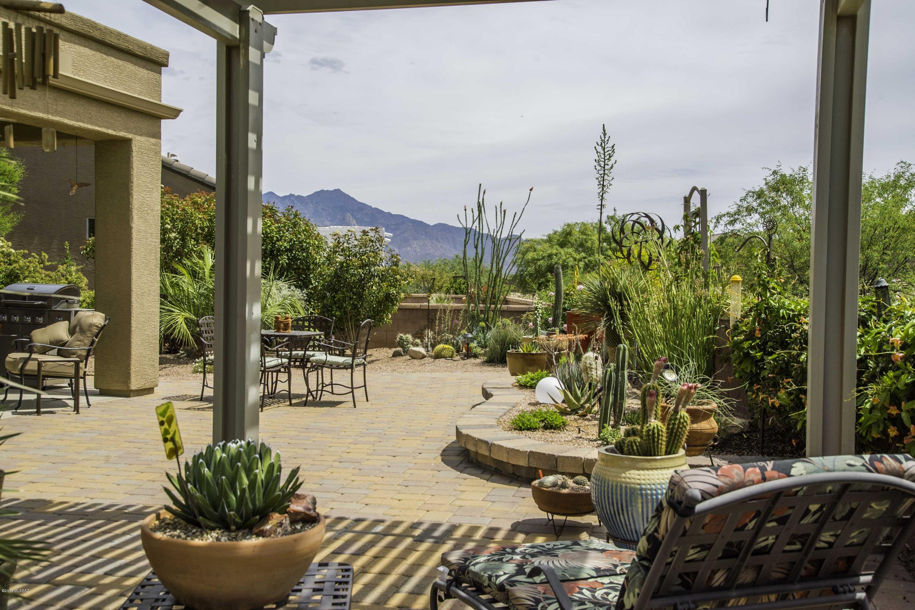 Twin giant palms amid an array of desert cacti provide great curb appeal and your front patio will provide views of the Santa Rita mountain to watch gorgeous sunrise and sunsets.  Enter into the great room with beautiful ceramic floor tile and an apportioned living space centered on a gas log fireplace with adjacent media/art niche.   Contemporary curved pony-wall architecture wraps the incorporated den for separation and relaxation.  The kitchen features attractive Corian countertops in warm earth tones with a custom tile backsplash, a Chef's gas range and under-counter stainless sink with a single handle gooseneck faucet.  The master bedroom suite is filled with natural light beaming through bookend windows while the bath offers comfort and space with separate his and hers vanities. Your outdoor patio lifestyle is enhanced by mountain views from an open-air Ramada where you'll can relax under a cool breeze.  A truly botanical experience displaying numerous vegetation species within island gardens surrounded by brick pavers and rock accents.  This adorable home sits in unique location on a larger, cul-de sac lot giving you the everything you are looking for and a bit more elbow room!