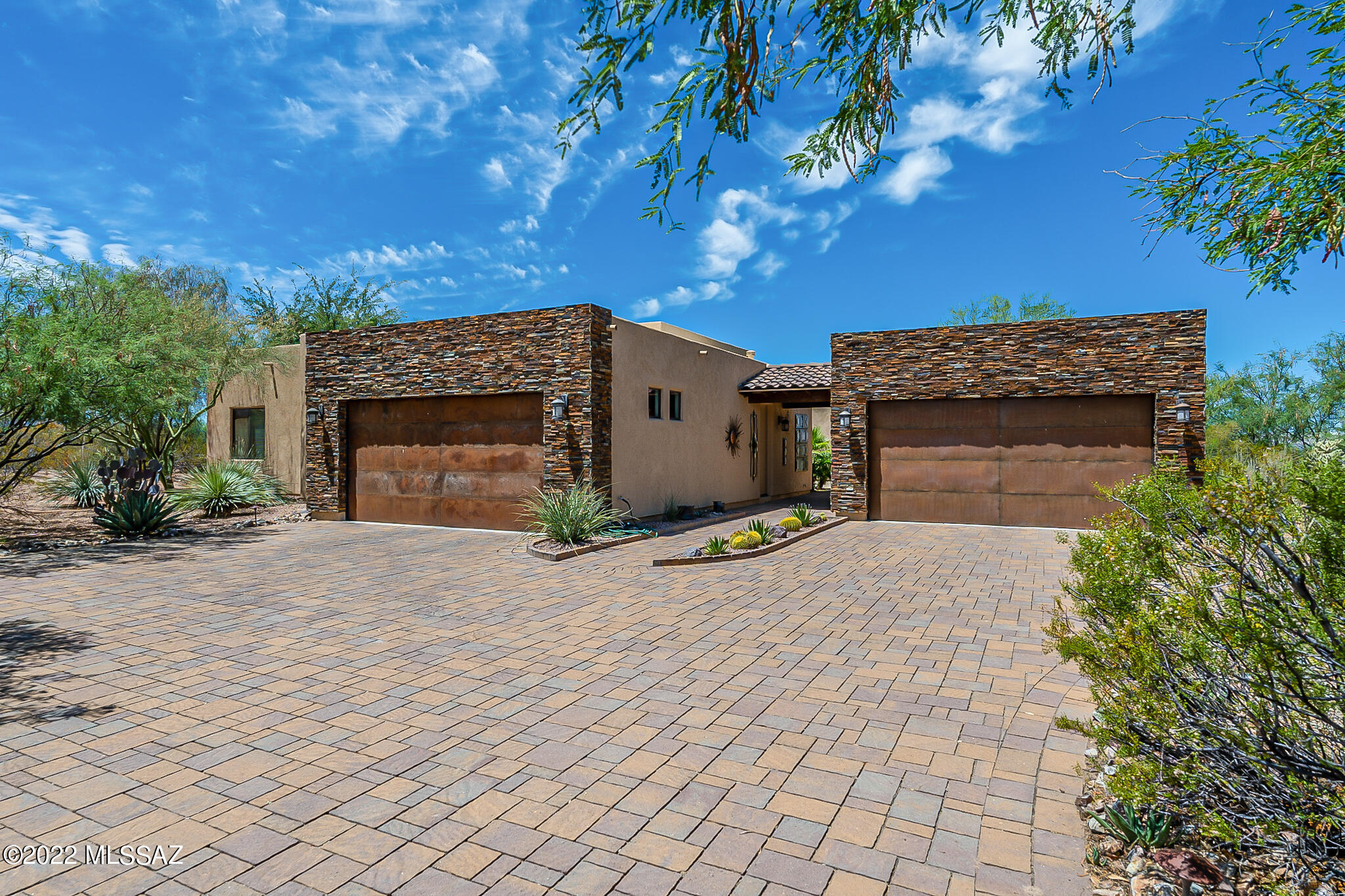 This stunning custom-built home is in the exclusive Stonehouse neighborhood and is situated on over a half an acre of land. The exquisite home offers stunning mountain views from the moment you enter and is 3740 square feet with four bedrooms, three full baths and two laundry rooms. There is lovely travertine tile throughout the main areas with cozy carpet in the bedrooms. The chef kitchen features granite counters, stainless steel appliances, double ovens, and Alder/Pecan cabinets. The open concept floor plan and 12-foot ceilings makes the main living area a magnificent space to entertain, relax or admire those gorgeous soaring Santa Rita Mountain views. The main suite offers executive height granite counters, dual vanity, glide-in shower, spa tub, and huge walk-in walk closet. There are two spacious guest rooms connected by a Jack and Jill full bath. The large third guest room ensuite has patio access and can double as a den or office. Four cars can be sheltered here!  There is a spacious attached two car garage and an additional detached two car garage that offers plenty of space for toys, giant workout room or hobby space of your dreams. Step out onto the large fenced private back patio to enjoy all the natural desert vegetation and spectacular mountain views.