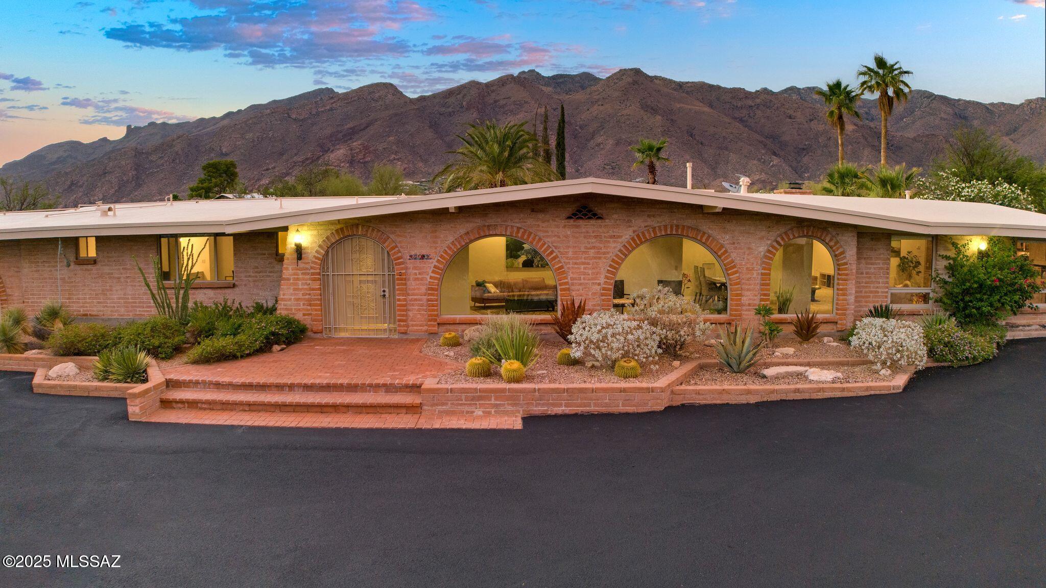 Imagine a personal retreat, far from the daily grind, where every day feels like a luxurious escape. This classic territorial-style home, nestled on over 1.5 acres in the heart of the desirable Catalina Foothills and District 16, offers just that. Enjoy serene mornings with coffee, relaxed afternoons with a drink, or delightful evenings dining with loved ones in the spacious north-facing backyard. Here, you'll be treated to breathtaking views of the Catalina and Tucson mountains, the gentle passing of local wildlife, and spectacular Arizona sunsets. From the front of the home, romantic city lights twinkle in the distance. Take a refreshing dip in the generously sized pebble tec pool, surrounded by swaying palm trees, vibrant oleanders, and thoughtful desert landscaping - a true oasis. This home is an entertainer's dream, boasting an open floor plan and a fabulous custom-built kitchen. The kitchen features granite countertops, ample cabinetry, a dedicated breakfast area, and brand-new appliances including a double wall oven, stovetop with retractable downdraft vent, microwave, and wine cooler, plus a newer dishwasher. For added convenience, a reverse osmosis system and water softener are included. Step into the expansive entry gallery, where arched windows and adobe brick masonry flood the hallway, living, and dining rooms with natural light, evoking a sense of timeless charm. A gas fireplace in the family room provides a cozy ambiance on cooler evenings. The versatile game/flex room, complete with built-in cabinetry, a bar, and pocket doors to the family room, easily transforms into an office, playroom, or entertainment hub. Travertine tile graces high-traffic areas, while soft, newer carpet adds comfort throughout the rest of the home. The primary bedroom suite offers a private retreat with a sliding door leading to the patio, built-in closet space, and a large walk-in closet off the bathroom, which features double vanities. The laundry room provides additional storage and a convenient half bath, perfect for pool guests. Outdoor amenities include a built-in gas BBQ and westside gate access to the garage. Beyond your private haven, you'll also enjoy access to the Skyline Bel Air Estates HOA community amenities, including a community pool, tennis courts, basketball courts, and a grill area. This property offers peace of mind with a freshly coated roof featuring a transferable 5-year warranty and a newer dual-zone HVAC system. The driveway has also been newly seal-coated. An attached list details all recent improvements.