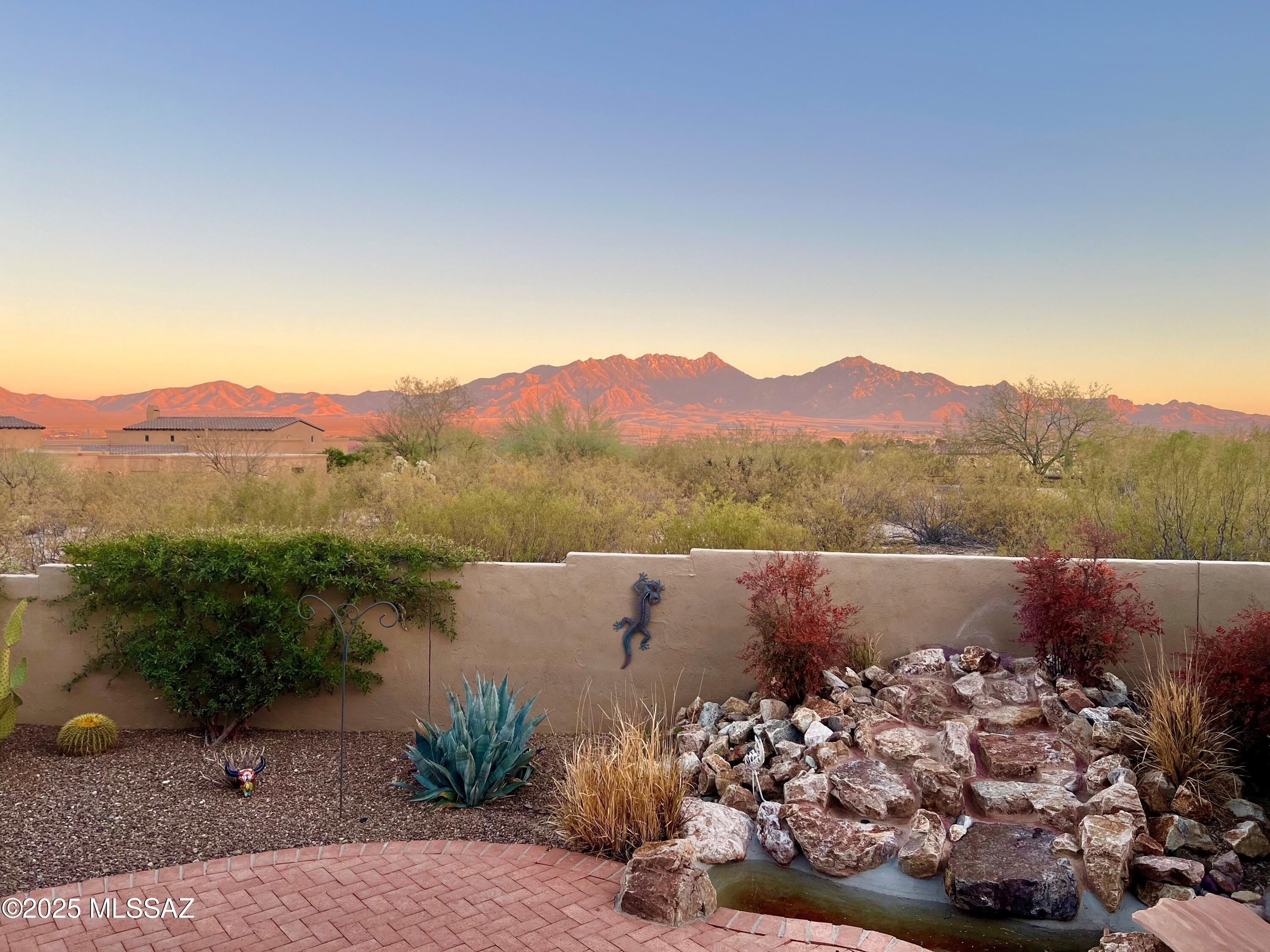 This exquisite home in a gated, non-age restricted community, offers panoramic mountain views and ultimate privacy on over an acre of natural desert landscape. A long brick paved driveway leads to a 3-car garage. Inside, enjoy tile floors throughout, with plush carpet in the bedrooms. The home features huge back windows, soaring ceilings, 8 ft solid wood doors, vigas and a striking beehive fireplace in the great room. Two primary suites each boast private baths. The kitchen showcases alder custom cabinetry, Santa Fe style ceiling beams, luxury granite and stainless steel appliances, including a wine fridge for entertaining. The formal dining room impresses with a coffered ceiling and tailored lighting. Privacy & luxury with stunning views combine in this must-see 
fully furnished retreat
