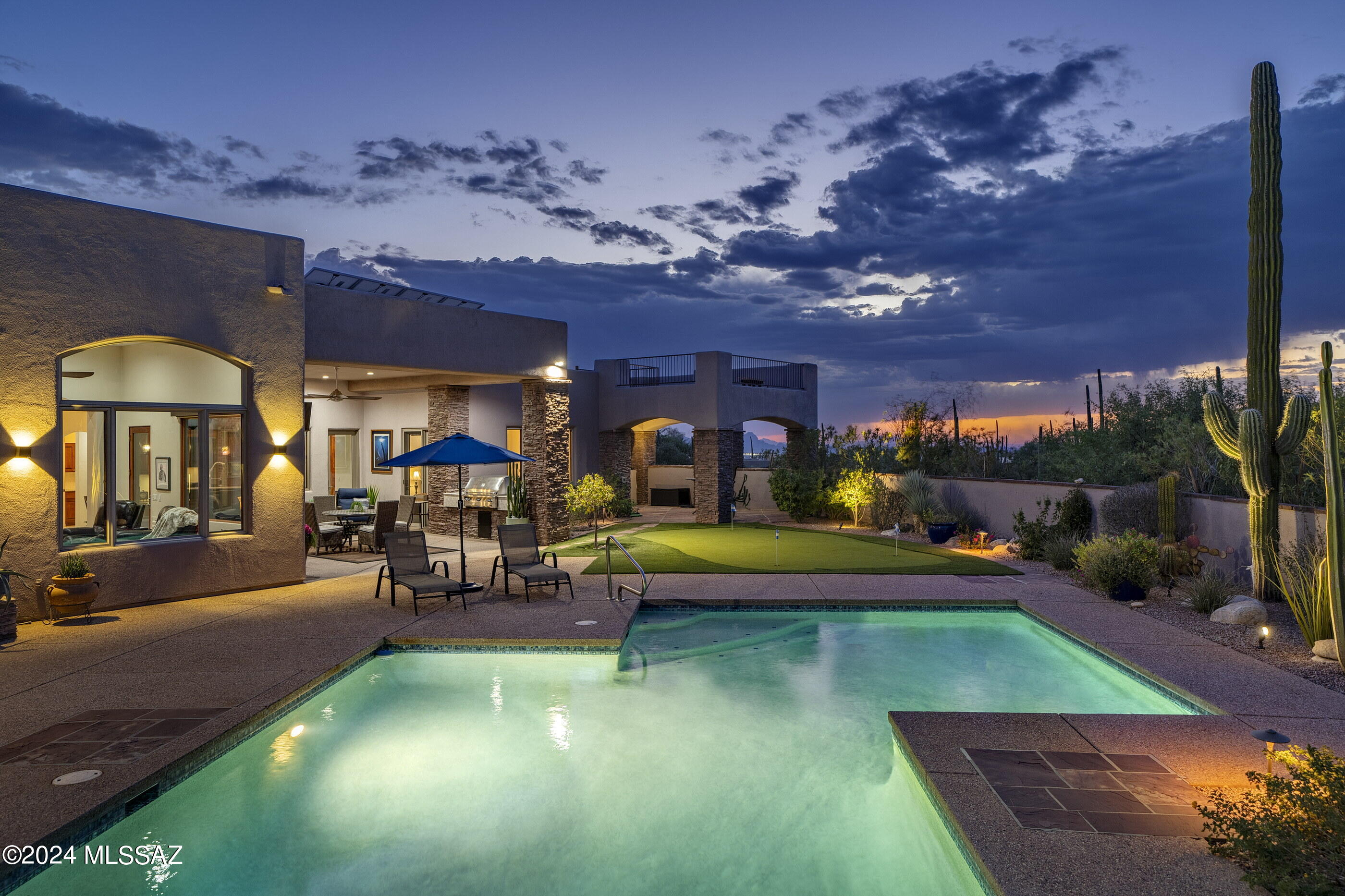 Located in the heart of Pima Canyon Estates, this traditional Southwestern home is designed to harmonize with the desert landscape, blending architectural form defined by stucco volumes, accented by natural stone cladding that anchors the home to its high desert surroundings. Deep roof overhangs provide both visual interest and practical shading, with North/South orientation reducing thermal gain while maintaining expansive, unobstructed views of the Catalina Mountains. Native plantings surround the structure, offering a visually compelling and low-maintenance environment, while enhancing the home's connection to its surroundings. Approaching the residence, the motor court is both functional and discreet, bordered by native mesquite trees and desert shrubs, which offer privacy without sacrificing the home's subtle elegance. The entry courtyard is served by a porte-cochère, creating a transitional threshold between the exterior and interior living spaces. Carefully positioned walkways of exposed concrete quietly reference the natural textures of the landscape, setting the tone for the interior experience, while guiding visitors toward the custom steel and glass entry door. 

Upon entry, the home's layout is organized around a central axis, emphasizing flow and sightlines that connect key living spaces to the exterior. Soaring ceilings accentuate scale, while large expanses of low-emissivity glass provide natural light without compromising energy efficiency. The interior finishes are refined yet restrained, with Travertine floors that float seamlessly throughout the space, juxtaposed against soft wall accents and materialsselected for their tactile qualities and timeless appeal. 

The kitchen exemplifies form and function, with custom cabinetry providing a warm backdrop to the space. Granite countertops and a seamless integrated backsplash offer visually uninterrupted surfaces, while high-end appliances are celebrated through thoughtful integration. A central island, topped with natural stone, serves as both a functional workspace and an informal gathering point, reflecting the kitchen's dual role as a culinary and social hub. Soft, indirect lighting enhances the material finishes without overwhelming the space.

The primary suite is designed as a private retreat, positioned to capture sweeping views of the Catalina Mountains, while ensuring the utmost privacy. The bedroom's proportions are generous, with floor-to-ceiling windows that blur the line between interior and exterior. In the en-suite bath, spa-like amenities are incorporated with a traditional aesthetic, featuring dual custom vanities, walk-in shower enclosure, and a freestanding soaking tub. The bathroom's design promotes tranquility through the use of natural materials, and a thoughtful layout that prioritizes the home's occupants. 

One of the property's many on-site amenities includes a fully integrated and privately owned electric solar system, representing a forward-thinking approach to energy efficiency and sustainability, while also reducing the home's operational costs.

The exterior spaces are as meticulously crafted as the interior, with the pool area offering a seamless continuation of the home's architectural narrative. An integrated pool and elevated spa reflects its surroundings, creating a visual connection to the distant mountains, while the adjacent terrace provides shaded outdoor living spaces through the use of deep cantilevers. Low-profile landscaping complements the architecture without competing with the panoramic vistas of the Catalina Mountains, which serve as a breathtaking natural backdrop. Discreet lighting enhances the space at night, allowing the views and architecture to remain the focal points for one to enjoy the Arizona Lifestyle.