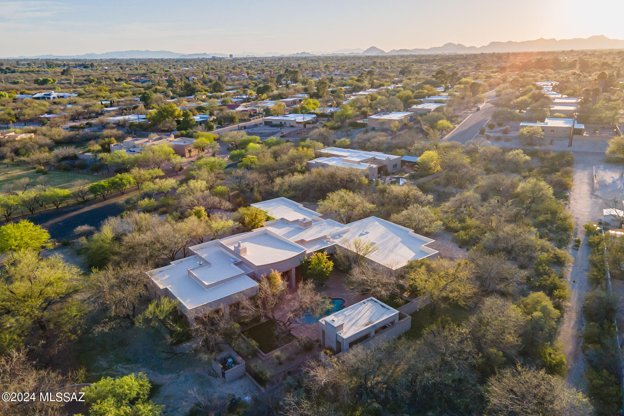 A stunning oasis of serenity, in a small and very private gated community, was designed by renowned Tucson Architect Michael Franks (who has designed homes in Tucson's most exclusive areas for over 50 years) ) to provide multi-functional indoor-outdoor living spaces that provide a seamless connection to nature. Richly landscaped with mature mesquite trees and stunning established desert plantings abounding throughout the 1.4 acre estate, this handsome abode includes the highest quality finishes in a quiet and serene setting perfect for entertaining or a multi-faceted family retreat. Spaces are grandly proportioned yet warm and welcoming. The generous use of oversized windows and glass doors allows for abundant natural light throughout the home. Entertain year-round on the multiple brick terraces overlooking the pool and spa and in the large cabana with its own stone fireplace providing a delightful space for serving drinks and canapes or even dinner. The backdrop includes views of the Catalina Mountains.  
A shaded courtyard entry adjacent to the broad circular drive accesses the home. The entry salon is grandly proportioned, with a high wood-beamed ceiling, large wood-burning fireplace with a handsome surround, and a curved bank of doors and windows leading to the multiple bricked terraces and walkways outside.  The heart of the home is the family room with a built-in  buffet,  handsome stone-surrounded fireplace, Taber & CO. mesquite floors and outdoor access, and the majestic well-equipped kitchen offering space for multiple chefs to create memorable meals. With striking granite counters, a six-burner + griddle Viking cooktop, two oversized refrigerators, custom cabinetry, a warming drawer in the large island with butcher-block surface and a large adjacent walkable pantry, this is an opportunity to hone your culinary skills (or call the caterer!)
A split-design floor plan discreetly places the four en-suite bedrooms and a guest den or playroom across the home from the primary suite. This owner's suite has direct access to the gardens and elegant pool, with a fountain just out the doors. The spa-like bath is a haven for relaxation, with a deep soaking tub, long stone-clad counters, and a separate make-up area. An adjacent closet facilitates his-&-her sections. 
The four-car garage includes attractive built-in storage cabinetry, a separate storage room, a workbench, and ample space for one's vehicle collection. A laundry room comparable in size to some NYC studio apartments includes a desk area and multiple storage options. 
With outdoor and indoor spaces thoughtfully positioned to provide comfortable spaces to gather, entertain or be private, all will feel welcome and comfortable here.