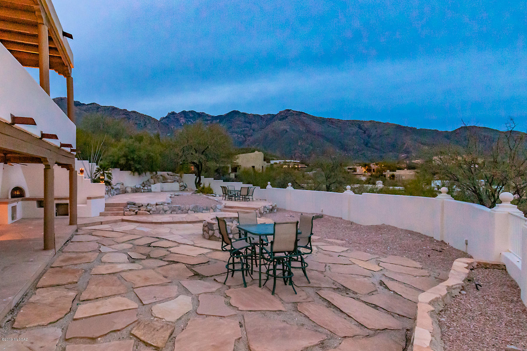 A spectacular Southwestern style home enjoying nearly 360* delicious views of mountains both close-up and wrapping around the Tucson Valley, gorgeous sparkling city lights, custom-built with walls of windows showcasing those views, is now available for the discerning homeseeker. Located In the desirable Alta Vista section of Tucson's famed Catalina Foothills, it offers abundant rich materials and finishes throughout: large-format flagstone flooring both inside and out on the many terraces, balconies and patios, elegant Venetian-style finishes on the thick stucco walls, Southwestern architectural details of vigas (wood ceiling beams), corbels (large wooden brackets supporting vigas), latillas (thin wood or cactus ceiling strips supported by vigas), lintels (wooden headers above windows and doors), and canales (protruding drainspouts), five interior fireplaces and another outdoors plus a huge stone firepit, an additional den downstairs with warm and inviting stone-surrounded fireplace, lots of spaces to gather with friends and family, intimate spots for relaxation and quiet conversation... truly a special residence. In the tradition and spirit of Southwestern architecture, the construction uses materials honestly so they become design elements themselves, and breaks down the barriers between inside and out. The star of the show is those views, down to Mexico and all over Tucson, as was intended by the owner, who designed this home for his family.
The tour starts up-on entering the rustic gate into the welcoming courtyard and being stunned by the views, which only get better by continuing around the balcony "parapet" that wraps the exterior of the one-of-a-kind home. The outdoor entry is a traditional "portal" in modernized form.  A dining room for those special occasions looks out over the Tucson Valley. A cozy living room has a deeply coffered ceiling, and provides a spot for quiet conversations, while the great room with its large beehive-style gas fireplace, bancos for casual seating, and walls of windows showcasing magnificent views is clearly the spot to gather and relax. The kitchen flows seamlessly and warmly from this comfortably spacious family room, with richly shaded and plentiful cedar cabinetry and a fabulous Garland stove and Bosch appliances. A bar seating area is hidden behind the Southwestern style pony wall. A huge island topped with butcherblock blends beautifully with the tumbled terrazzo counters and backsplash. The adjacent oversized laundry area is also a pantry with room for a substantial wine fridge. Two generously sized bedrooms with walk-in closets and an attractive full bath are adjacent. The master suite has a romantic kiva-style wood-burning fireplace (enjoy the fragrance of that mesquite on a cool evening!) tucked into a corner and doors providing views both North and South. An elegant master bath includes a generously sized Jacuzzi tub set upon a travertine surround, travertine surfaces throughout, elegantly separated vanities, and a walk-in shower with multiple water outlets and sprays to delight the senses. A walk-in closet has room for his and hers. 
Downstairs is an entire suite of possibilities, with a den focused on a large stone-surround fireplace, a substantial wet bar with seating and room for a small fridge, lots of room for a pool table, and a bonus room that could be a terrific media room, office or workout space. Also downstairs is a well-sized guest room with its own fireplace and full bath. Outside is a huge curved terrace outfitted with a large stone firepit and another kiva-style fireplace or horno            (based upon a traditional outdoor oven to bake bread), and room to entertain a crowd while enjoying sweeping sunset views. The city lights in the evening are memorable! This home has been lovingly cared for and maintained by the original owners and is now ready to be enjoyed by a new generation. With famed Catalina Foothills District 16 schools and easy access to the best of Tucson's shopping, dining, entertainment and medical facilities, this property clearly meets the "Location, Location, Location" test. Please call for your private showing. Al, 520-488-6088 or Sandy, 520 488 8318.