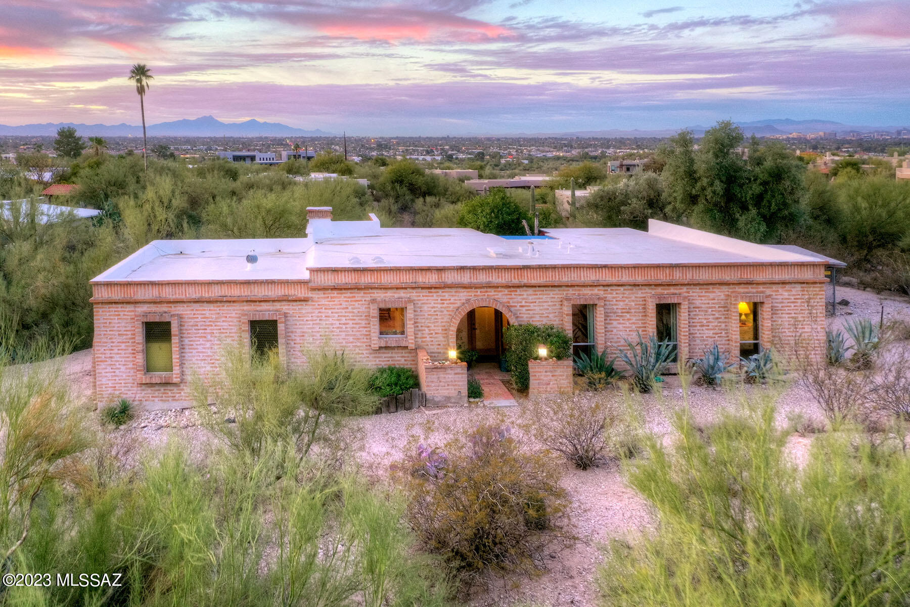 Flecha Caida Burnt adobe Territorial home.  Owned and renovated by the current over for almost 50 years.  Beautiful stained concrete floors in the living areas.  Cork floors in the kitchen & den.  Exposed wood beamed ceilings, kiva fireplace archways, built ins are a few of the charming architectural features of this lovely home.  Remodeled Gourmet's Kitchen w/stainless steel appliances, seam foam green tiled backsplash, custom wood cabinetry, break fast bar.  Primary bedroom has remodeled ensuite bathroom with walk in shower.  2nd bedroom is ample.  Charming backyard has covered patio, brick pavers, & spa overlooking desert, city lights & mountain views.  2 car garage! on approximately .84 acres of land!  Close to the River Walk, The JCC and more!