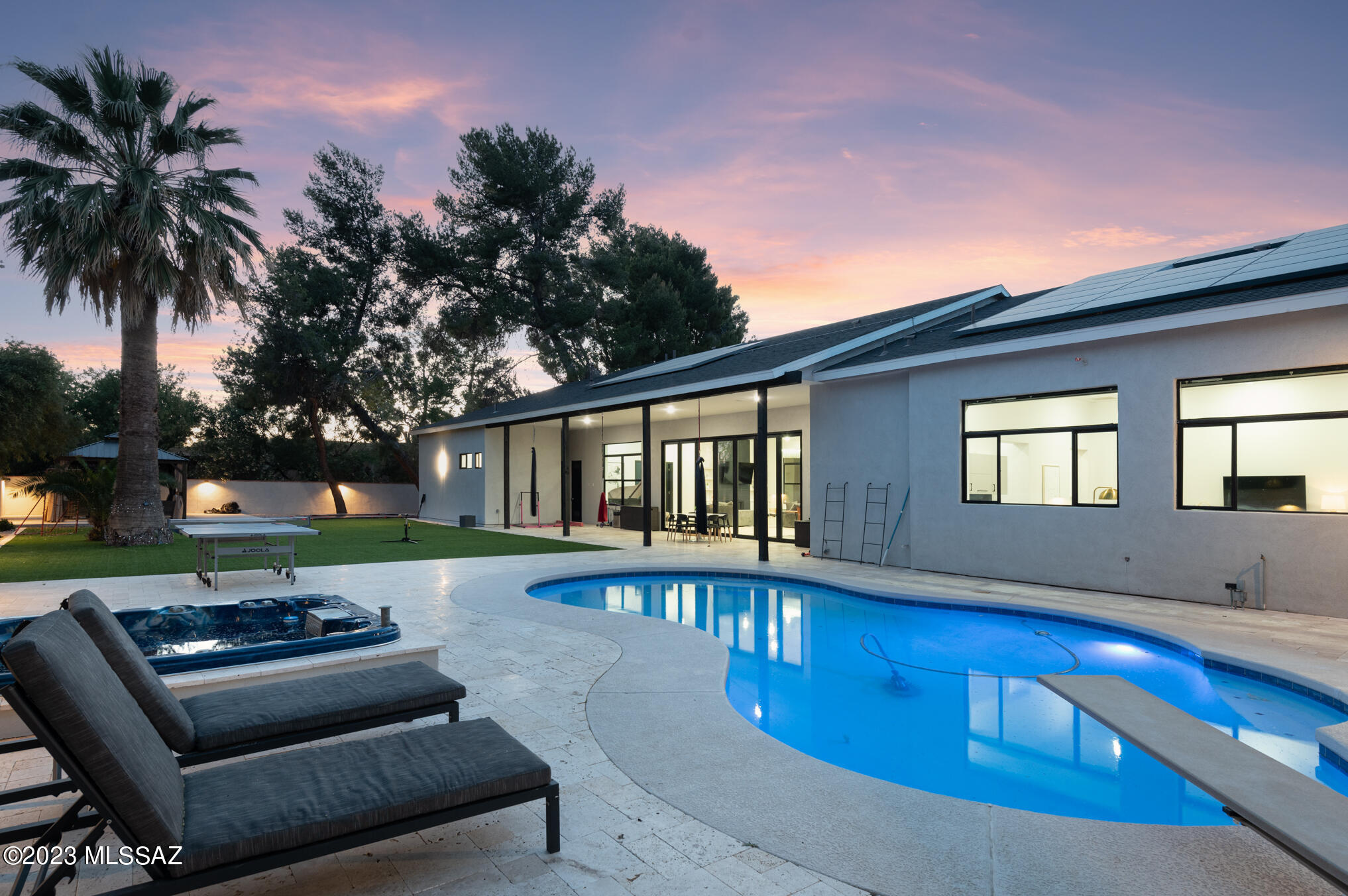 Located in high-demand, guard-gated Tucson Country Club Estates, this expanded & completely rebuilt modern home has it all. New Tesla solar panels compliment this home built for ease of use & efficiency.  Over one thousand square feet has been added & the roof has been raised for high ceilings at this sprawling, modern home. Every inch of the interior is new including floors, cabinets, countertops, appliances, fixtures, custom lighting, paint, doors, windows, trim & more.  Experience modern life in style w/ thoughtful design that creates seamless indoor/outdoor living. The grounds provide endless opportunities to have fun in the outdoor spaces without the huge cost of maintaining grass. A newly walled & gated front yard with a huge turf lawn is large enough to host a soccer game. The covered front patio,  w/ travertine pavers offers magnificent views of the mountains, creating a picturesque setting. Custom front door leads to an impressive entry that is light & airy & gives way to the spacious great room w/ soaring ceilings & a wall of windows showcasing the backyard. Massive center island w/ breakfast bar anchors this well-executed modern kitchen & serves as a gathering point for family & guests. New cabinetry w/ desk & floating shelves, quartz counters & backsplash & Thermador stainless steel appliance package that includes large refrigerator, freezer & beverage cooler. Dream pantry w/ custom built-ins, space for small countertop appliances & cereal bar. Dining area adjacent to the kitchen can be used for large-scale entertaining both formal & informal.  Fireplace w/ custom built-ins & floating shelves serves as a focal point adding warmth to this large space w/ sectional couches for spending time with family & friends, watching TV or playing games. The split bedroom floor plan offers a master suite wing that is a private & luxurious retreat . Spacious office w/custom built-ins leads to the master bedroom that offers a relaxing space to unwind.  The master wing features his & hers closets & bathrooms.  Spa-like his bathroom has a double sink vanity, gorgeous quartz countertops, custom tile surround over-sized shower w/ smoky glass enclosure. Her closet, w/ a built-in center island dresser,  is a huge one-of-a-kind paradise for those who love all things clothes, shoes, bags & accessories.   Access her bathroom through her closet for supreme privacy. The other wing of the home is comprised of four bedrooms, three and a half bathrooms & a bonus room w/ a wet-bar that can be used as a teen suite, kids playroom, workout room, additional office or whatever suits your needs. Powder room off entry is convenient for guests & expresses a bold style in-line w/ the overall aesthetic of the home. A huge laundry room near the garage is a has distinctive tile floors & corresponding backsplash, plenty of storage.
The backyard is in a class by itself, with vast & dynamic spaces built for enjoying & being active outside.  A massive, deep-covered patio protected on both size feels like an extension of the great room & more living space. It is the perfect place to host a dinner or gathering. Two turf lawns are separated by a pool w/ a diving board & a built-in hot tub. Timeless & functional travertine pavers cover the pool deck. Trampoline built-in to the ground has colorful under-lighting. Gazebo in the corner of the yard provides yet another covered gathering space.  New roof, HVAC & garage w/ plug-ins for 2 electric cars.  New Tesla solar panels convey.