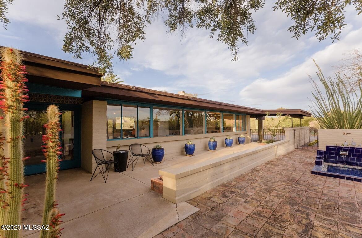 Pictures don't do this home justice- it's a must see! Come fall in love with this stunning Tom Gist historic, Mid-Century modern, Catalina Foothills estate.
This classic stunner is set atop a small hill and at the end of a cul-de-sac where you can bask in the panoramic mountain and city views that will follow you indoors with breathtaking wall-to-wall windows. Our gorgeous Sonoran desert enwraps the 1.24 acre property and follows you up to the front door with captivating cacti, ocotillo, and trees, all native to this beautiful and serene habitat. Outdoor space abounds with a Palm-Springs picturesque pool, opposite a tranquil water feature, patio space for entertaining and morning yoga. Wraparound patios provide abundant space for all your potted plants and those hummingbird feeders. Inside you will find period-appropriate fixtures....with updated lighting, custom design paint and MCM wallpaper, remodeled kitchen, where you can wash your dishes with a view, remodeled master bathroom, warm vibrant tones and tile throughout with wood-burning fireplace and solid wood doors providing that Hacienda vibe. As was customary for the distinguished Tucson builder, Gist built this home to feature an elongated floor plan, large view-oriented window walls, ribbon street-facing windows, and burnt adobe construction. All of this character finished with modern-day energy efficiency...owned solar! This makes enjoying those walls of windows and sparkling pool a little sweeter! Come see why this 4 bed/3 bath 2,467 sq ft one-of-a-kind home makes you feel like "This is Tucson"!