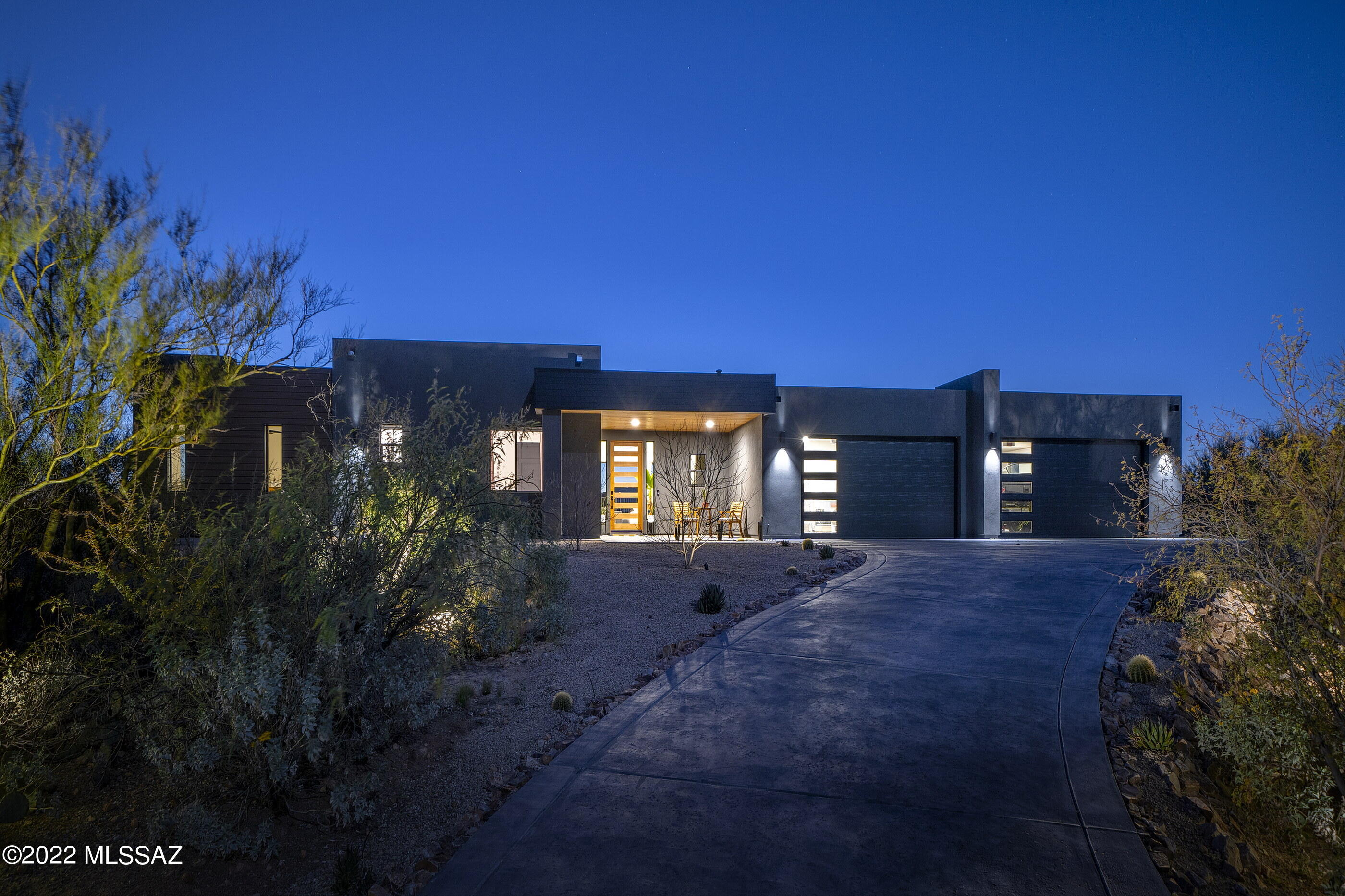 Stretching boldly across this commanding home site, situated at the highest nearby elevation and spanning the width of two central view corridors, the arrival sequence of this striking contemporary home creates a visual juxtaposition that embraces both the native landscape, while contrasting the architecture designed by Stephen Bohn and constructed by Terra Cotta Building and Development. The delineation point between contemporary design and the natural desert landscape, emphasizes the beauty of nature against the shape and form of the stuccoed and clad structure, producing a strong graphic both horizontal and vertically. Upon entry, the view extends into the great room giving the space a sense of lofty expansiveness... while allowing natural light to sweep in and the eye to move past the folding glass doors, out onto the rear veranda. 

The kitchen features custom millwork, with soft shade gray cabinets and drawers dressed in honey bronze hardware, set against a naval blue center island that carefully choreographs the users movement through the space. Exposed concrete floors line the interior, threading the living spaces together, providing continuity to the overall design. The floor plan, while open, features a split bedroom makeup, with the owner's suite privately sequestered on the North end of the residence, with the balance of secondary suites situated on the South end. 

Floor to ceiling retractable glass walls spill out onto a back veranda, connecting the refuge of the home with the exterior living spaces. The pool, being the centerpiece of the backyard, draws in the surrounding mountain ranges, with the ever-changing skyline reflecting off the water's surface.