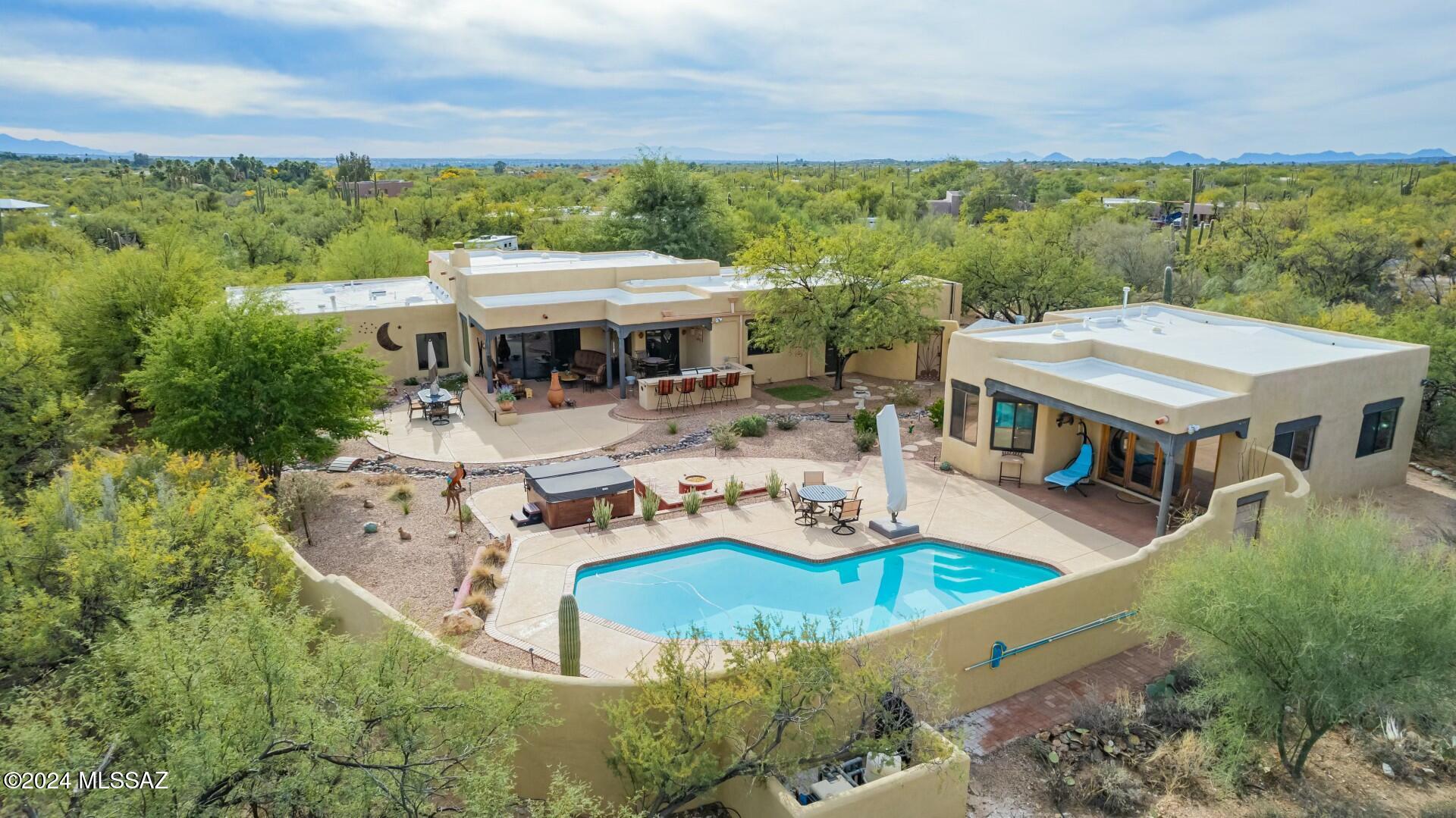 Your dream home awaits in the serene Makoho Estates of NE Tucson. Meticulously maintained Santa Fe-style home on 1.01 acre, horse property, Mountain Views, no HOA. Indoor/outdoor living, 3 bedroom, 2.5 bath plus 1 bed, 1 bath 771 sq. Ft. casita. 
Exterior: landscaping, patios, outdoor kitchen, heated pool and spa. Interior: chef's kitchen, Saltillo floors, high-end baths, new doors and more. Two car garage and workshop attached to main home. Privacy abounds on just over one acre of beautiful desert horse property, positioned to maximize the stunning mountain views.
Upon entering the fully-paved driveway, you will be welcomed by mature, native desert landscaping leading to a welcoming gate beckoning you into the newly-designed courtyard patio adorned with seating areas, fountains and lush landscaping. Follow the brick path which leads to striking new arched, double wrought iron doors. Once Inside, you'll realize the special feel this home offers, as your senses take in the spectacular views from your great room. Beautiful new Saltillo tile floors complement the viga beam ceilings and a stunning turquoise-inlay mesquite fireplace mantle atop your floor to ceiling, wood-burning fireplace aside new sliding glass doors to the back yard, which allow for true indoor/outdoor living. 
The West wing of the home features a dining room, breakfast nook and chef's dream of a kitchen, outfitted with WOLF appliances, a large, steel farmhouse sink, birch cabinets and granite countertops. The custom wall-length pantry cabinet is spacious and offers soft-close doors and pull-out shelves. The laundry room is equipped with a utility sink, storage closets, and an updated half bath. Convenient access to the two-car garage and separate workshop are also situated on this side of the home. 
Moving to the East wing of the home, you will enjoy a spacious primary suite and two guest bedrooms. The main bedroom is spacious, offering a separate sitting area and features new sliding glass doors, offering stunning mountain views through a private patio area. The primary bathroom is a showpiece which displays spectacular mesquite cabinets, new marble counters and a relaxing walk-in shower. The mesquite cabinets, marble counters and saltillo floors are echoed in the other bathrooms, rounding out the high-end feel of desert luxury in the main home. Additional interior features include new shades and window coverings on each window and designer paint throughout. 
Outdoor living is unparalleled, with a heated pool accented by a serene waterfall feature, new cool decking and a luxurious above ground hot tub. A cozy fire pit and raised privacy walls create a resort-style oasis. Your guests can enjoy privacy and comfort in their own 771 square-foot guest house, which has one bedroom, a living area, one bath and kitchen. Schedule your private showing today.