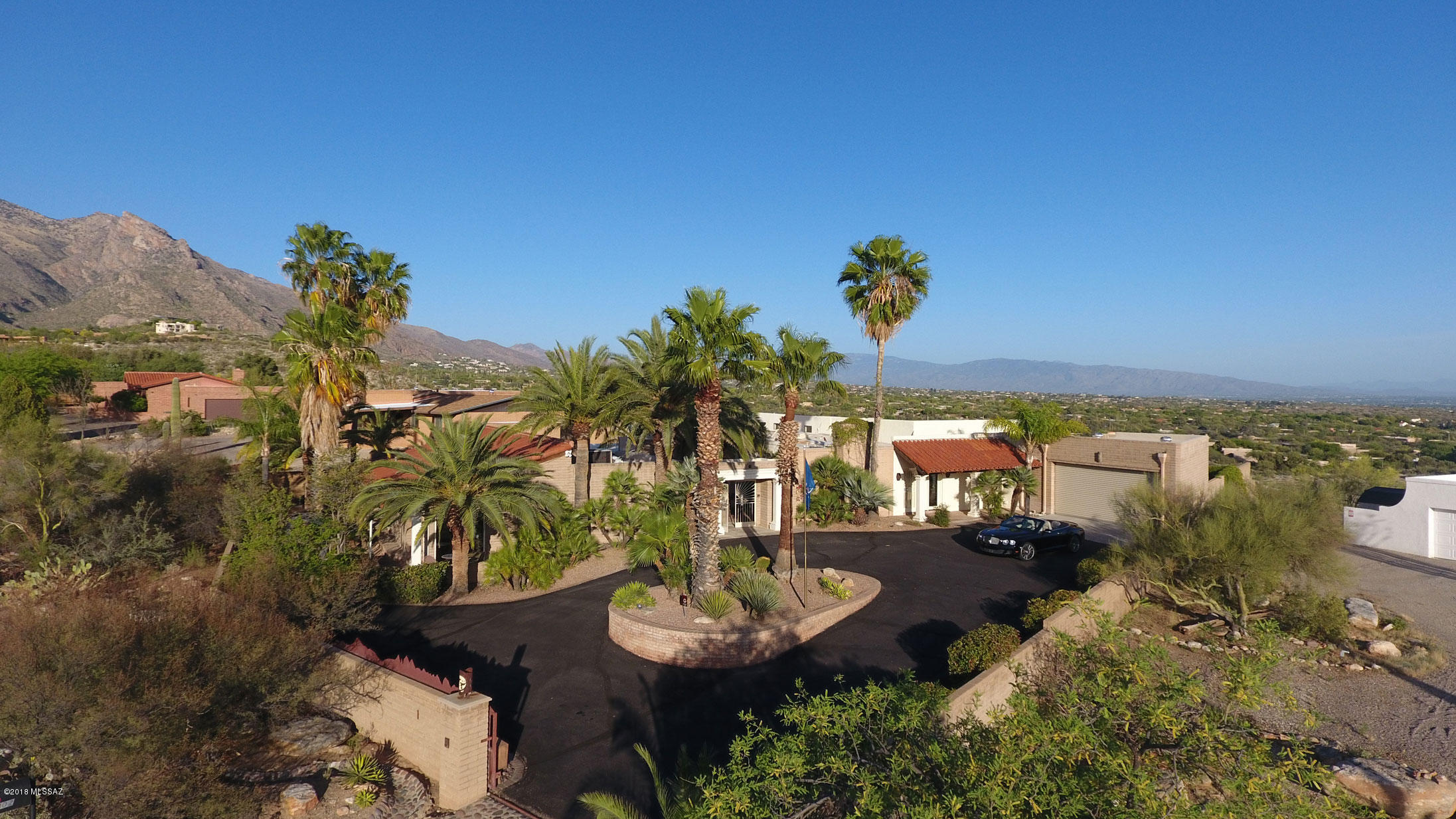Majestic ancient palm trees grace a broad circular driveway leading to the gated courtyard entry to a truly magnificent Foothills home. Picture multiple sweeping flagstone terraces and patios with wrap-around views of Tucson's many mountain ranges, close-enough-to-touch panoramas of the Catalinas and a gorgeous turquoise pool overlooking Tucson's sparkling city lights. Add to this a fabulous, impeccably maintained elegant home boasting custom travertine inset floors, multiple wood-burning fireplaces in and out, room to entertain a crowd or raise a family in comfort and pleasure, plus walking distance to La Encantada for dining, shopping and galleries, and walking distance to Manzanita Elementary School, one of Tucson's best elementary schools. A spacious entry hall leads to private flagstone patio, a generous formal living room with a large stone fireplace, and a gracious dining room with doors and windows providing more gorgeous views and access to yet another flagstone patio. The open and flowing kitchen-great room-breakfast area- bar is fabulous, with views over the terraces and pool to the Rincon Mountains, downtown Tucson and the Santa Rita Mountains. Doors are screened to allow cool breezes to flow through the living area. The kitchen and bar area have richly shaded granite counters which continue into the full butler pantry and adjacent powder room. Pull-out drawers enhance the alder cabinetry in the kitchen, bar and butler pantry. Handsome stacked stone columns accent the area, as do pendant lights over the counter bar. The stainless-steel kitchen sink provides instant hot water and cooled filtered water. The full butler pantry provides additional storage, a second dishwasher, stainless-steel sink and microwave. A small powder room is adjacent, also with granite counters and alder cabinetry. A large laundry room has space for crafts or projects and includes an additional refrigerator. The garage is also oversized and provides yet more storage. 
The true "piece de la resistance" of this spectacular home is the outdoor area, a mÃ©lange of flagstone and brick covered and open terraces, planters and irrigated lawn spaces on multiple levels, an outdoor kitchen and a handsome wood-burning fireplace, all surrounded by pueblo brick walls that echo the natural desert colors and set off the perfect elegant turquoise pool. Not to mention the up-close-and-personal views of the famed Finger Rock formation of the Catalina Mountains from this totally private area. Watching the city lights start to turn on at sunset is a mesmerizing meditative experience, sufficient to make your heart sing. On a clear day, or night, you can indeed see forever, or so it seems. Call the caterers, bring on the string quartet and let's have an event! 
Yes, there's more inside to enjoy. The spacious master suite includes a large stacked stone surrounded fireplace, a generous sitting area, a walk-in closet fit for a Princess (just add sparkly chandeliers!), another private patio and a substantial executive office with handsome built-in shelving and doors out to another private enclosed courtyard patio. The master bath is amazing, with rich charcoal granite counters and raised tub surround and as accents in the travertine floors, all reflected in walls of mirrors. Watch the sun rise onto Finger Rock while brushing your teeth! A large walk-in shower provides FOUR shower heads and a bench. Three additional large bedrooms are located down a separate hall, one with an en-suite bath and another full bath for the other two bedrooms. And did we mention LOCATION, in the middle of everything, with easy access to downtown dining and entertainment, excellent medical services, and just a few minutes to the best middle school and high school in Tucson? SO, what are you waiting for? We would be delighted for you to preview this fabulous home TODAY!