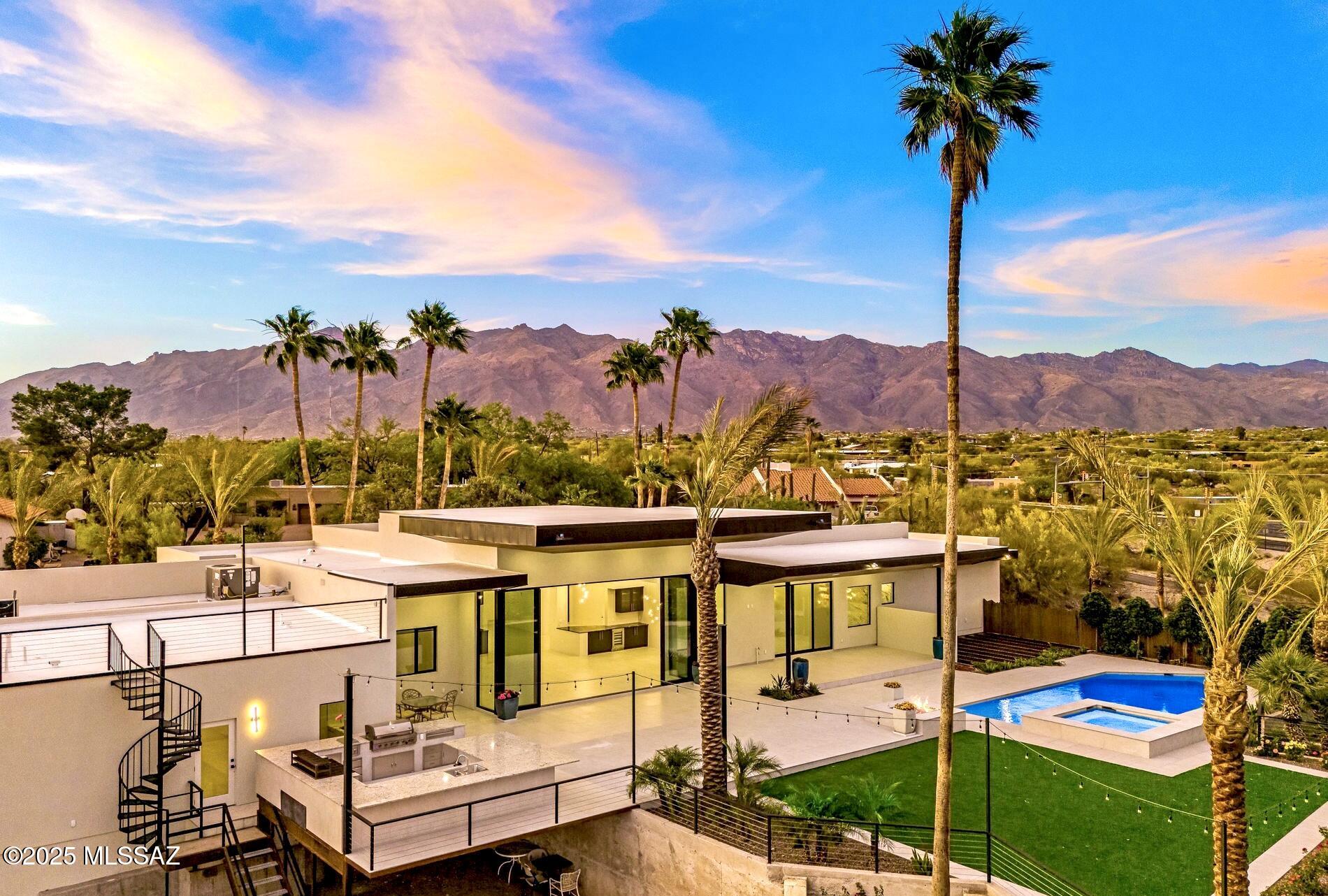 Discover unparalleled luxury in this newly constructed modern masterpiece, nestled on over 2 acres of pristine land in the coveted Catalina Foothills. With no HOA, a private well, and a modern aesthetic, this exceptional property offers the ultimate in sophistication and freedom.
 
As you arrive, a circular paver driveway lined with a grove of mature olive trees welcomes you to a stunning glass pivot entry door. Showcasing the impeccable craftsmanship of master builder Monty Bartholomew, this 4,541 sq ft estate includes a 4,000 sq ft main house and a 541 sq ft attached casita, designed for seamless multi-generational living. The casita features its own entrance, kitchen, bathroom with dual vanities, and laundry, ensuring complete independence. Step inside to a world of sophistication, where Fleetwood windows, including a 6-panel multi-slide door in the great room, blur the lines between indoor and outdoor living. The chef's kitchen is a culinary dream, boasting double ovens, a gas range, separate Sub-Zero refrigerator and freezer, dual sinks, a massive island with ample seating, a secret pantry, and dramatic granite countertops illuminated by drop ceiling lighting. The adjacent dining area dazzles with glass bar cabinetry and a wine refrigerator. Electronic window shades and ceiling speakers in entertaining areas enhance the ambiance, while 24" x 48" porcelain tile flooring flows throughout, offering beauty and low maintenance.
 
The spa-inspired master suite is a sanctuary, featuring a soaking tub, rain showerhead, breathtaking views, and Taj Mahal quartzite countertops. Each of the four bedrooms includes an ensuite bathroom with tiled showers, quartz countertops, and LED mirrors. A media room/office, four full bathrooms, a powder room, and a pool bath complete the interior.
 
The backyard is a showstopper, with unobstructed mountain and city views of downtown and "A Mountain." Dive into the heated pool and spa, controlled via a phone app, or gather around the massive gas fire pit. The expansive outdoor kitchen is an entertainer's paradise, equipped with two refrigerators, a built-in BBQ, a wood-fired mesquite grill, a gas burner, a sink, and abundant bar-top seating. Mature imported palm trees, lush landscaping, café lights, and a large artificial turf area create a resort-like oasis, perfect for pets and play. A spiral staircase leads to a rooftop deck, offering panoramic views of the entire city. A cleared area awaits your visionideal for a pickleball, tennis, or sports court.
 
With a 6-car garage (2-car on one side, 4-car tandem on the other), there's ample space for your RV, toys, or car collections. This spectacular property, free from HOA restrictions, is a rare opportunity to own a luxurious, modern estate with unmatched views and amenities in the heart of the Catalina Foothills. Don't miss your chance to call this extraordinary home yours.