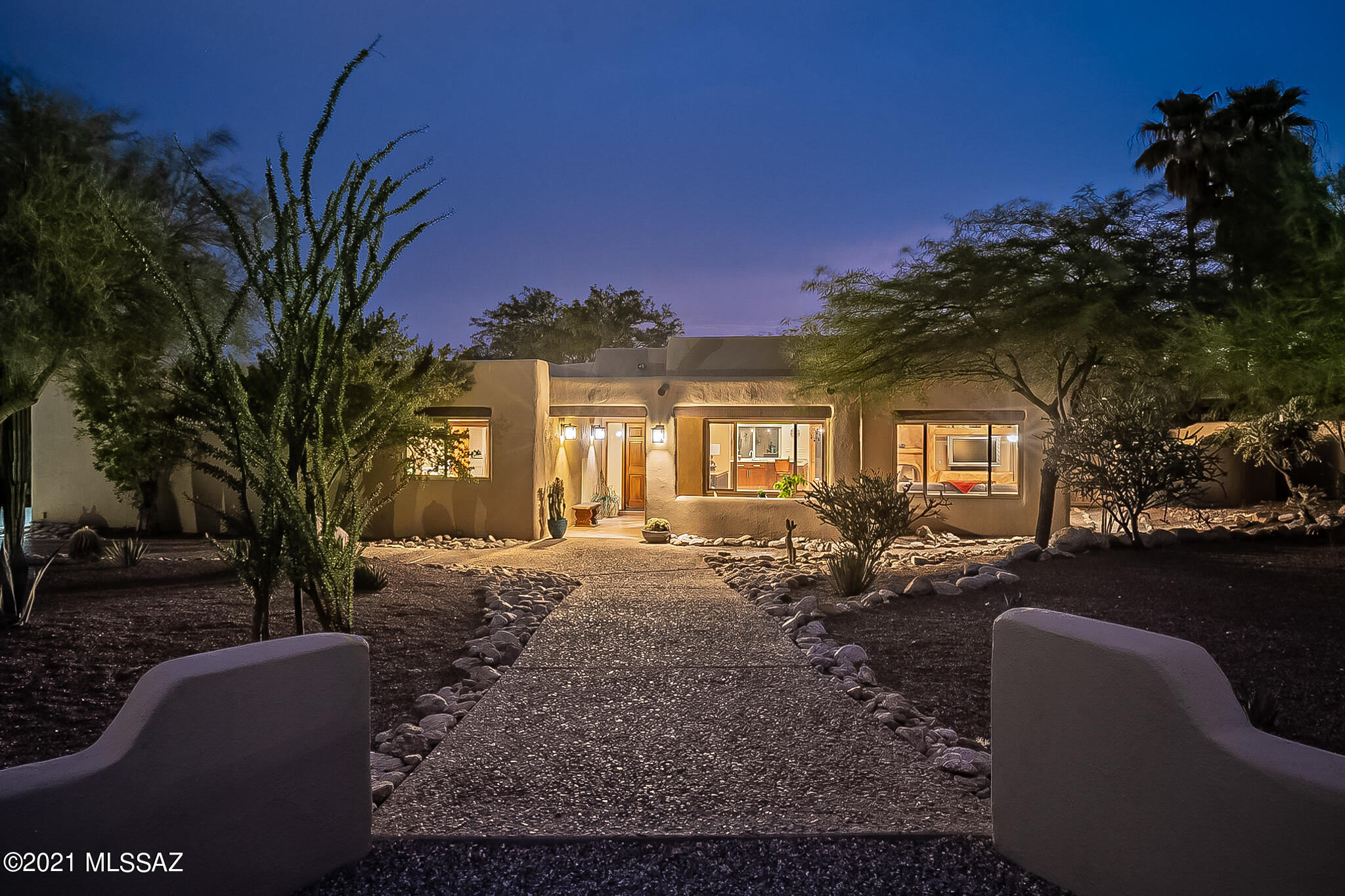 A Santa Fe style haven in Shadow Hills, with a fantastic open plan, a rare combination of feel and features, and a southwestern charm that instantly feels like home.  Its unique combo of space and layout can easily host the largest gathering without losing a bit of intimacy.  The light-filled great room soars, with viga/plank ceiling and an artfully painted three-sided fireplace that anchors the home without feeling imposing.  Thoughtfully designed and perfectly executed custom features at every turn.  Indoors and out, the space, flow, and ambience here are unmatched.  A huge primary bedroom suite, secondary BRs ideally situated for guests and office, without a single interior step...all enveloped by the verdant natural surrounds of Shadow Hills.  Full Vid & 3D virtual tour are a must-see. Not all square footage is created equal--just as not all "great rooms" are great--but there can be no question that, with a great room that earns every bit of its label, and with a rare combination of light, flow, space, all grounded with an easy, natural feel, this home lives larger than expected. 
There are so many thoughtfully added and well-done touches throughout, it's hard to know where to begin.  Starting in the great room, a wall of built-ins, with custom stained concrete countertop, a cabinet-door-faced wine fridge, and a bench window seat, allows for a buffet for serving holiday festivities or extra storage for the everyday (and a space large enough for multiple extra tables and seating).  Above, a beautiful viga and plank ceiling, with custom track spot lighting.  An impressively done three-sided fireplace provides centering point for the space, and a hub of warmth and energy during the "winter" months.  Though capable of burning wood logs, this wonder of a fireplace is plumbed with natural gas, as well, and is easily imagined as a center for winter-season warmth, family, and friends.  Across from the fireplace a custom wet bar, with an under-counter fridge of its own, bar-height seating at perfect conversation space from the kitchen, and plenty of storage for glassware and occasionals.  The kitchen, too, lives, works, and hosts bigger than what one would expect in a home of this size.  A U-shaped kitchen workspace, with gas cooktop, plenty of granite countertop surfaces, and open to the main living areas, is every bit a part of how this home lives, hosts, and plays so much larger and better than one would expect of a home of this size.  Accented by under-cabinet lights, the horizontally- arrayed backsplash is of hand-crafted glass tile, of a depth and intricacy that required a skilled specialist to install.
On the dining-space side of the kitchen, an outward-facing run of lower cabinets, with plenty of extra storage to make hosting easy and hassle-free.  An enormous picture window fills the space with light, perfectly sized to parallel a dining table.  
From the kitchen, the flow leads one past a well-situated wall of additional pantry cabinets toward bedrooms, perfectly laid out, with one bedroom split off to the eastern side of the home, and the second bedroom/office and primary bedroom suite on the south side.  The primary bedroom suite impresses, with a wall of built-in cabinetry for clothing storage, and recessed built-in shelving for artwork, photos, and deco pieces.  On the southwest side of the bedroom, a large window soaks the room in Autumn and Winter's afternoon light.  On the other, leading toward the en-suite bath with dual vanities, a well-appointed and high-ceilinged walk-in closet (outfitted with  shelving system from California Closets).  For convenience, the primary en-suite bathroom adjoins the laundry room (and through it, the hallway back to the kitchen), which allows for a circular flow and adding to the surprisingly spacious feel of the home, in both its appearance and function.
The third bedroom is perfectly set up to serve as home office or den, with its own southwest-oriented window to soak in cool-season light, green vistas, and desert blue skies.  In the left-most closet, a built-in shelving system (also from California Closets), and in the right?  A full-sized fold-down Murphy bed perfect for easy hosting overnight guests.  For the many who prioritize a home office, the easy-to-use bed allows this 3 Bedroom home to live more like a 4.  On the eastern side of the home, the second bedroom, with a window that welcomes the morning light and a generously sized closet as well.
Guests enjoy a spacious and well-renovated hallway bath, with italian marble tile floors, a glass-top basin sink, and a huge air-jet-equipped bathtub.

 It's been thoughtfully renovated over the years, with attention paid to detail and systems.  It should be noted that the three highest-cost replacements endemic to so many 35+ year old homes in the Foothills have already been taken care of here: the roof has been replaced and re-worked to prevent ponding, the HVAC replaced with a Trane system, and all of the windows in the home replaced with Milgard dual-paned windows with work done by Olander's.  The water heater was replaced in 2021.  The concrete floors throughout the living areas, too, have just been refinished in August 2021 (after listing photos were taken).  

While all of those features are enough to fall in love with, the outdoor living spaces are superb in their own right.  In front, an east-facing courtyard and intimate covered patio, perfectly sized for a cafe table, a cup of coffee, and enjoying the sun rising over the desert natives (ocotillo, agave, and a massive multi-armed saguaro).  On its tree-shaded western side, the home opens at three points to the covered patio and the privacy and lush natural beauty of a low-walled back garden.  The border between this back yard/patio and natural desert is just well-defined enough, with a low wall that sets the interior managed space apart from the wild half, without blocking the energy and wonder of the natural area beyond it.  With just the right amount of shade from Palo verde and Mesquite, an expansive flagstone-surfaced area allows for multiple areas to sit and host, whether for outdoor dining or around the outdoor firepit.  Under the rich viga and planked porch roof, a built-in stainless steel gas grill, and plenty of room for sofas AND for tables and seating atop the freshly painted surface.  The convenient laundry-area door comes into play here, too, as a natural path for guests to transit to the hallway restroom without having to navigate the kitchen.  

With pathways that lead through gates on either side of the home, there's a generous feeling of space and flow all around. 
A perfect blend of natural aesthetics, beautiful surrounds, and feature-rich interior spaces that have been renovated and outfitted to maximize enjoyment, this home stands apart from the rest.  And set as it is in the heart of one of Tucson's most coveted neighborhoods, it will no doubt prove a treasure for whomever is lucky enough to call it "home."