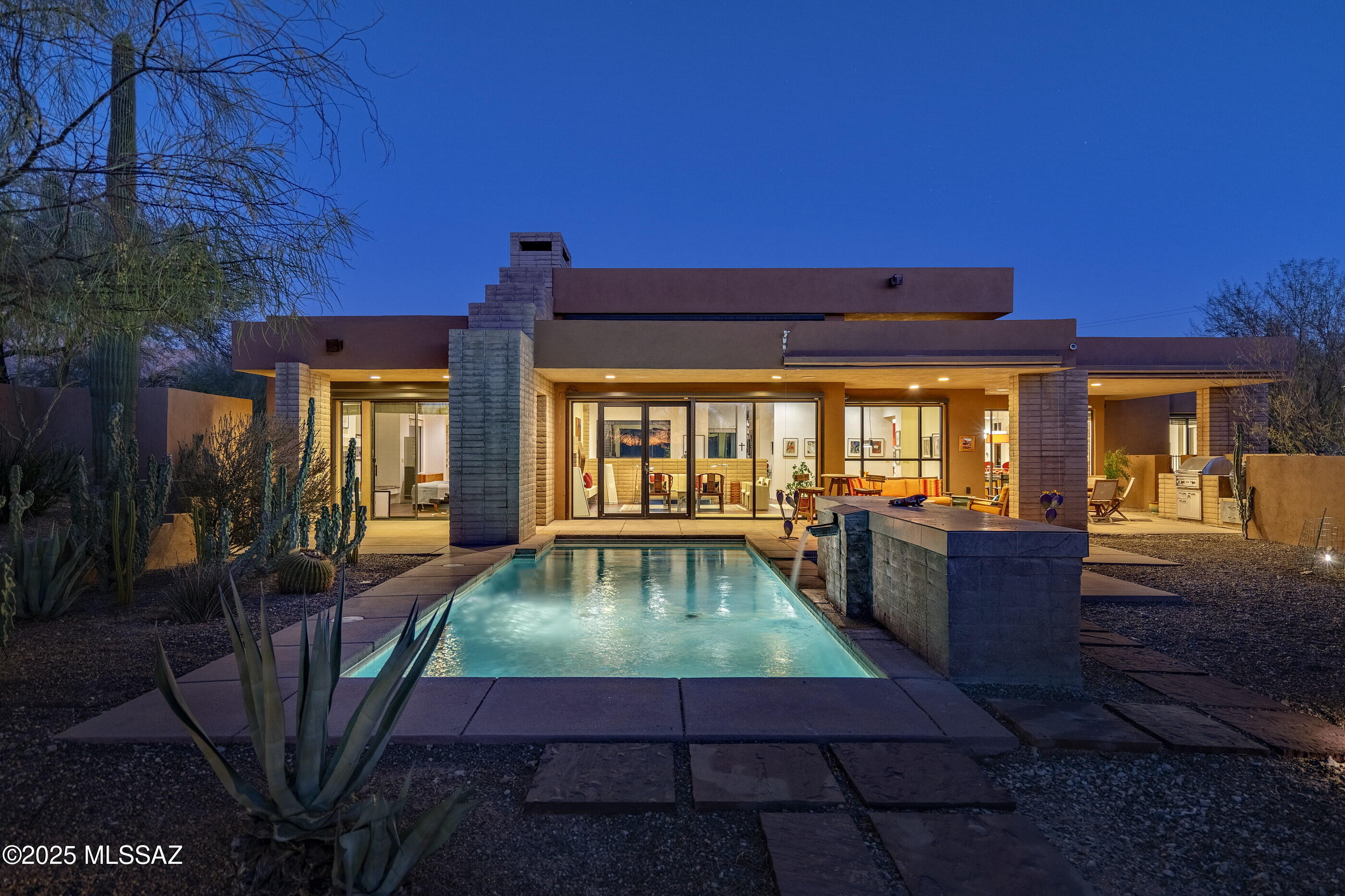 Nestled within the heart of the Catalina Foothills, this Kevin Howard design emerges as a quiet retreat emphasizing simplicity, calmness, and the harmony of space and light, where the architecture integrates seamlessly within its natural surroundings. Designed to embrace the essence of the desert landscape, the residence is thoughtfully oriented to capture soft, filtered natural light, which pours into the great room through expansive glass façades. From the moment you step through the glass entry, you are immersed into a cinematic experience that unfolds as the evening sunset casts dramatically over the pool and spa, grounding the home in its setting. The residence flows effortlessly between interior and exterior spaces, blurring boundaries and extending the scale of the home outward. Each programmatic element is meticulously considered to heighten the experience of living within the Tucson desert lifestyle.

The kitchen, a centerpiece of functionality and design, reflects clean contemporary lines that echo the home's design language. Smooth natural stone countertops offer both beauty and practicality, while custom rift oak millwork integrates seamlessly, creating a warm yet modern aesthetic. Positioned to flank the great room, the kitchen becomes a space of connectivity, bringing people together while maintaining an understated elegance. Tile flooring extends throughout the interior, creating visual and material continuity that unifies the design. The owner's suite, located in its own private wing on the north end of the residence, is a retreat unto itself. Featuring a walk-in dressing closet and a spa-inspired bath with a large soaking tub, walk-in shower, and floating dual vanities. On the opposite end of the residence, two generously proportioned secondary en-suites provide comfort and privacy for family or guests, creating a thoughtful split bedroom floor plan.

Floor-to-ceiling glass walls open onto a covered veranda, seamlessly connecting the home's interior refuge with its exterior living spaces. The backyard, anchored by a pool and spa, becomes a focal point for reflection as the water mirrors the ever-changing desert skyline. Every detail of the home has been crafted with precision and purpose, resulting in a space that exudes ease and elegance, offering both a lifestyle of comfort and a venue for unforgettable moments of connection and celebration.