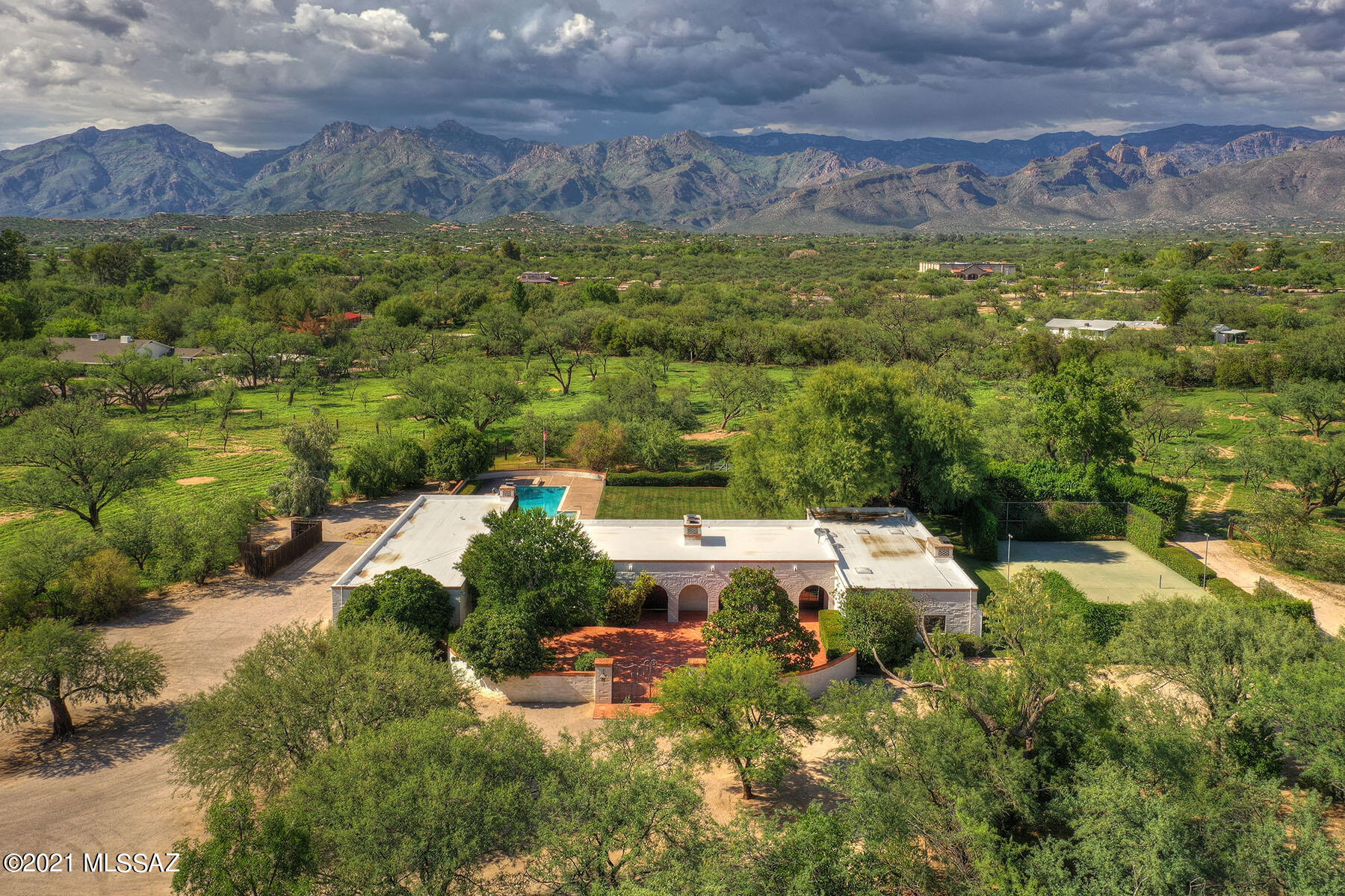 Timeless, Classic Burnt Adobe built by Master Builder Kesterson. Situated on 9 AC on secluded Woodland Road.  One owner home is original, but has been well cared for through the years.  Lovely courtyard entry with  old wrought iron gates from Tucson Country Club. Magnificent Great Room has high, beamed ceiling, sliding doors on two sides, masonry fireplace and Teak Wood Floors. Elegant Formal DR features a paneled wall w/ hidden cabinet space. Great kitchen has  brick floors & large laundry/ pantry area. Two master suites + den/office in the main house.  Full guest house w/ fireplace & kitchenette. Fabulous back porch for entertaining a crowd, screened in porch, plus open porch.  Delightfull swimming pool, lush landscaping & paddle tennis court. Private Well. A WONDERFUL OASIS!