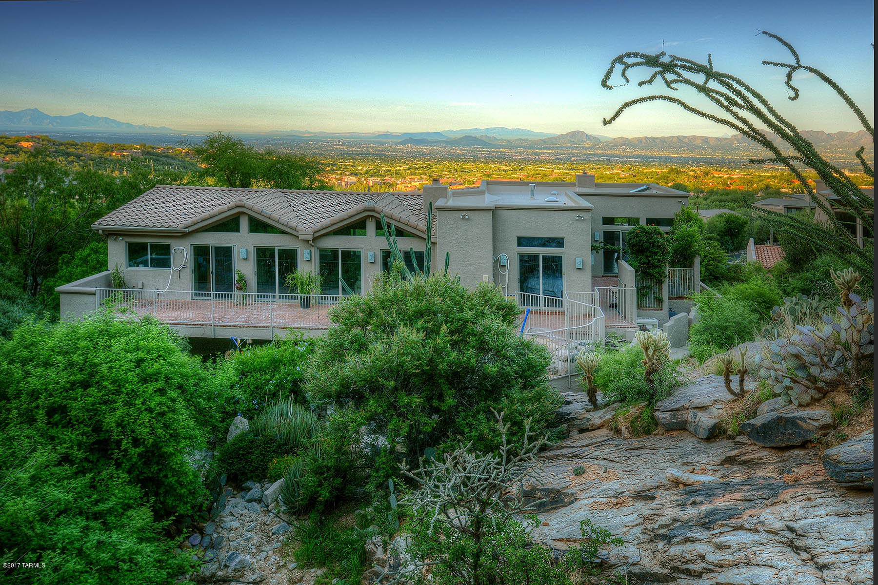 High behind the gates of Sin Vacas you find this home literally nestled in the heart of the Catalinas sitting on 21.56 acres as its backdrop. Make your way to a private driveway lined with mature natural vegetation of high country desert. Upon entering you may visit a private master suite on the first floor, just ideal for visiting guests. Then, depending on your preference, take the brick lined stair well or the elevator to the second floor where you will find a second bedroom & another master bedroom w/fireplace & spectacular mountain & city views. On this second floor we find the living room & dining room in a great room setting spanning & hydrologist inspired steel bridge over the canyon wash. Come visit & commune with nature at every turn. Borders Pusch Ridge wilderness area.
